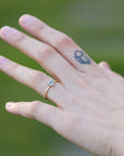 Hand with a gold ring and a small tattoo on a blurred green background