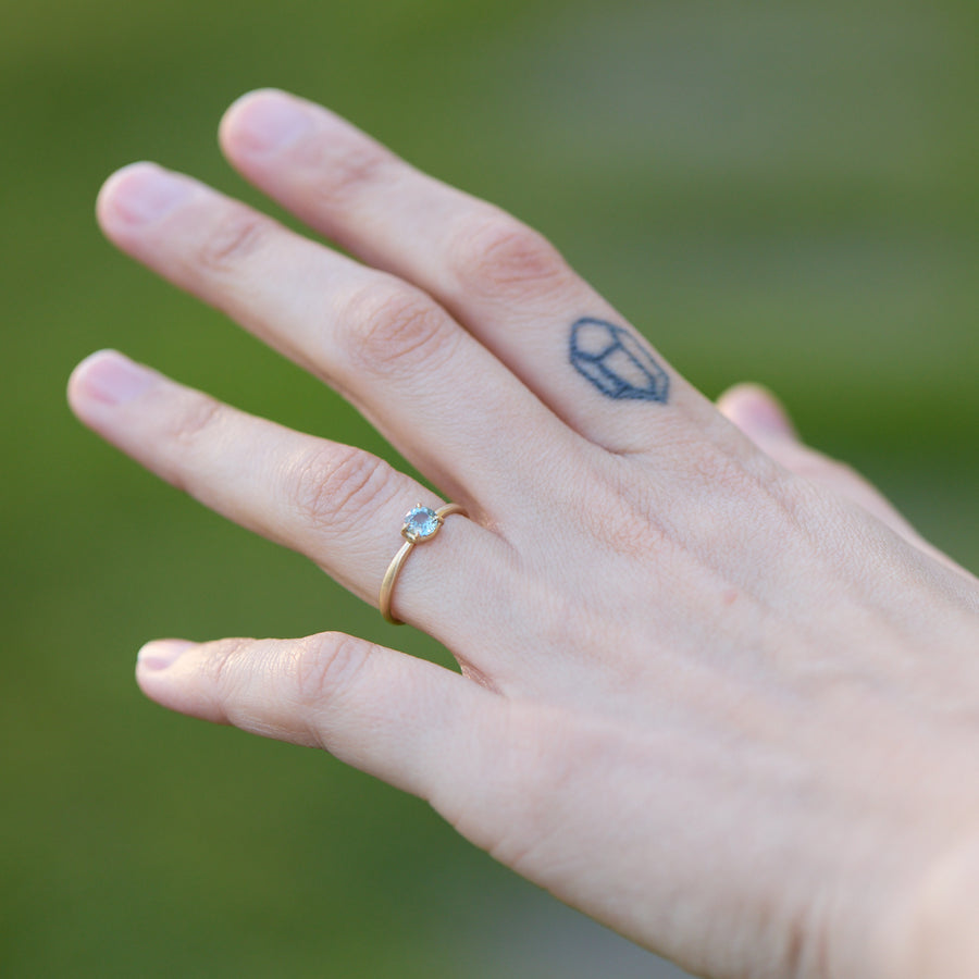 Hand with a gold ring and a small tattoo on a blurred green background