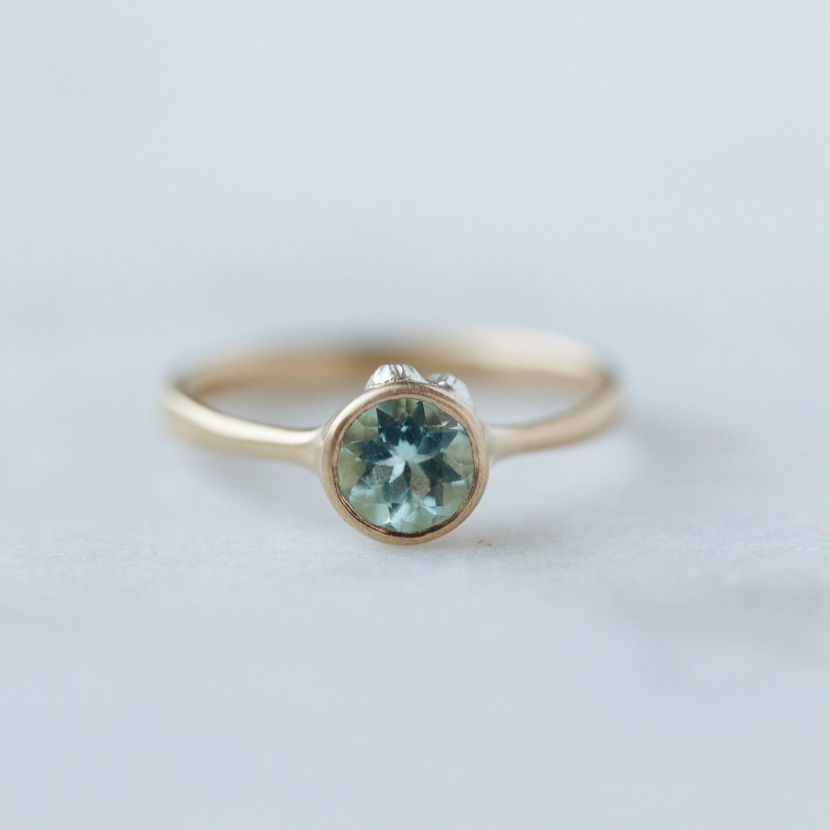 pale green round emerald set in gold bezel ring with silver barnacles. Front view.