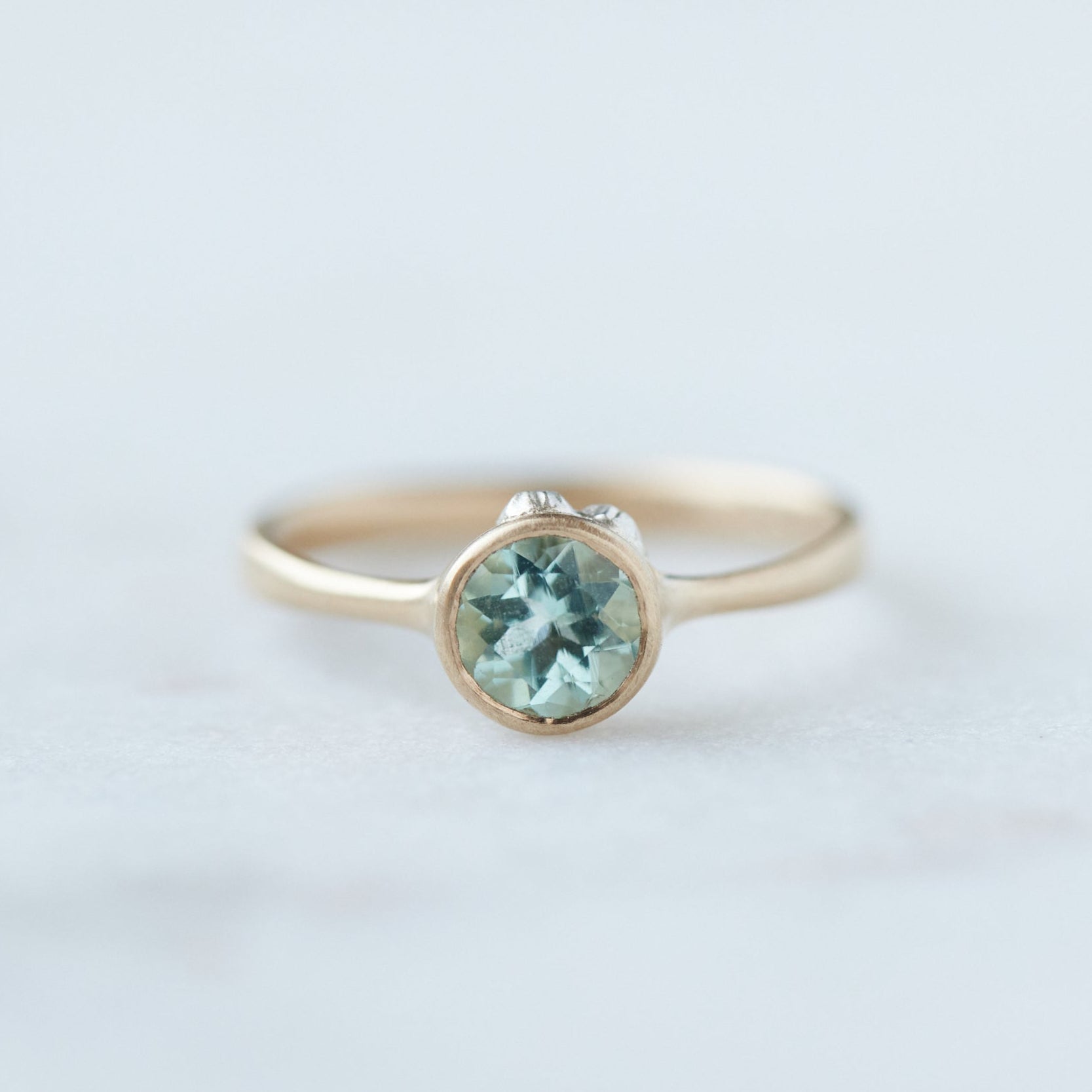 pale green round emerald set in gold bezel ring with silver barnacles. Front view.