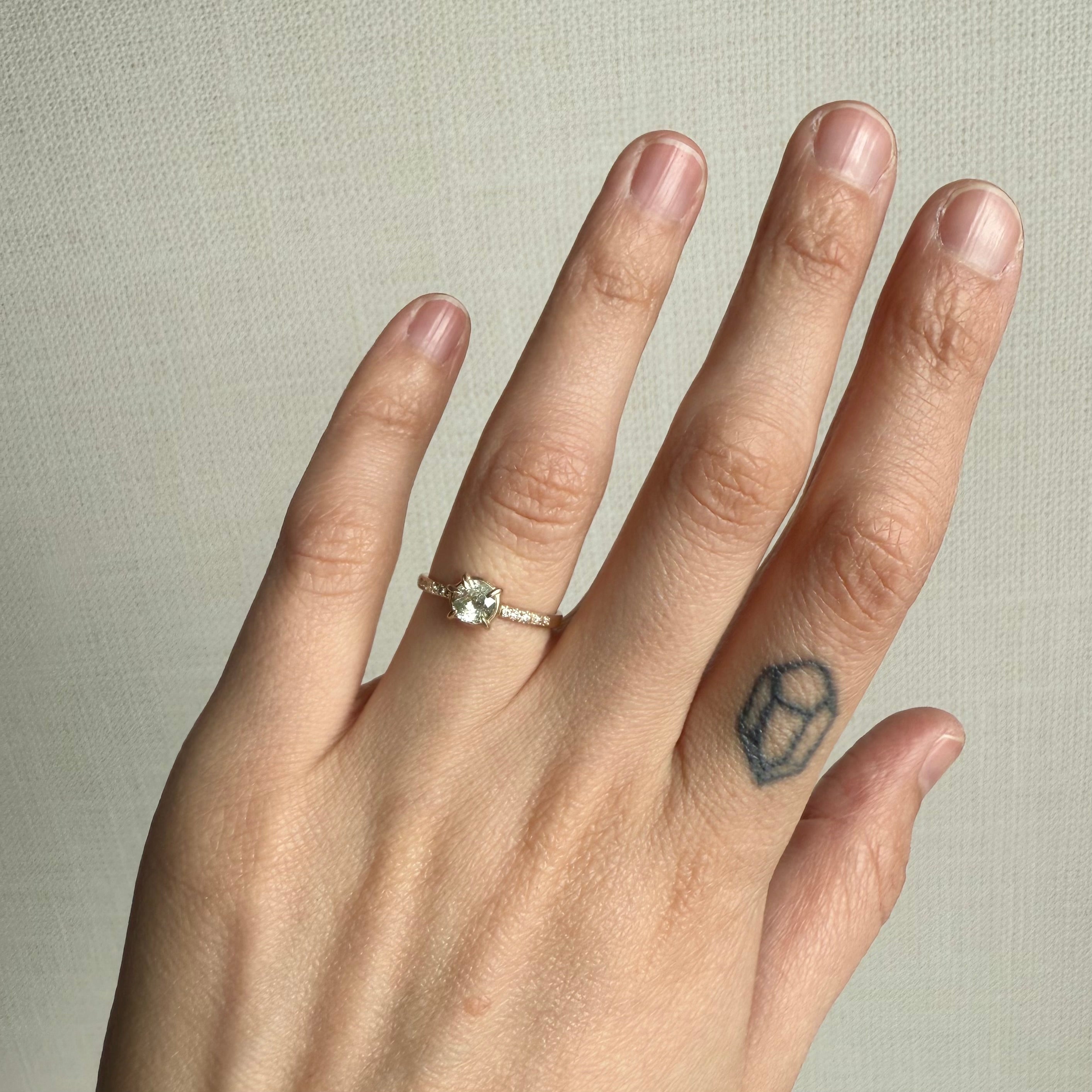 Hand wearing a ring with a small white stone ring on a neutral background