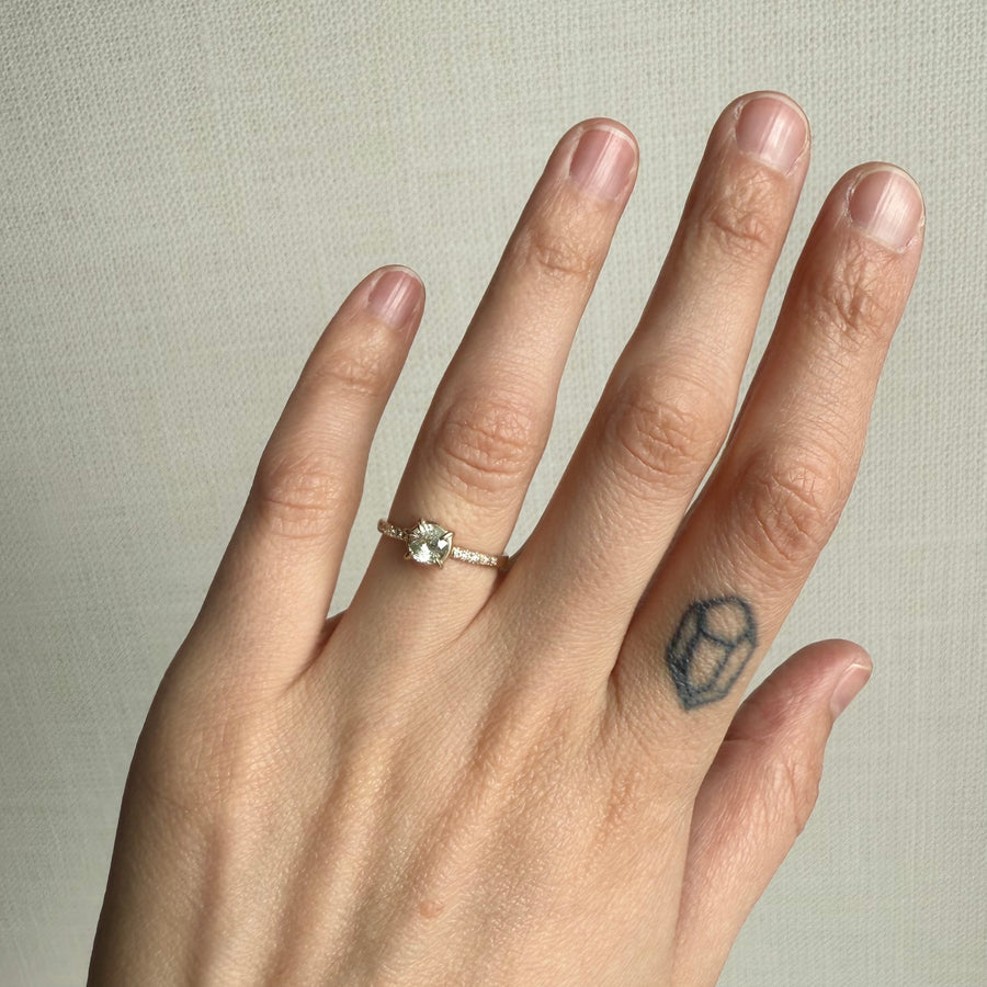 Hand wearing a ring with a small white stone ring on a neutral background