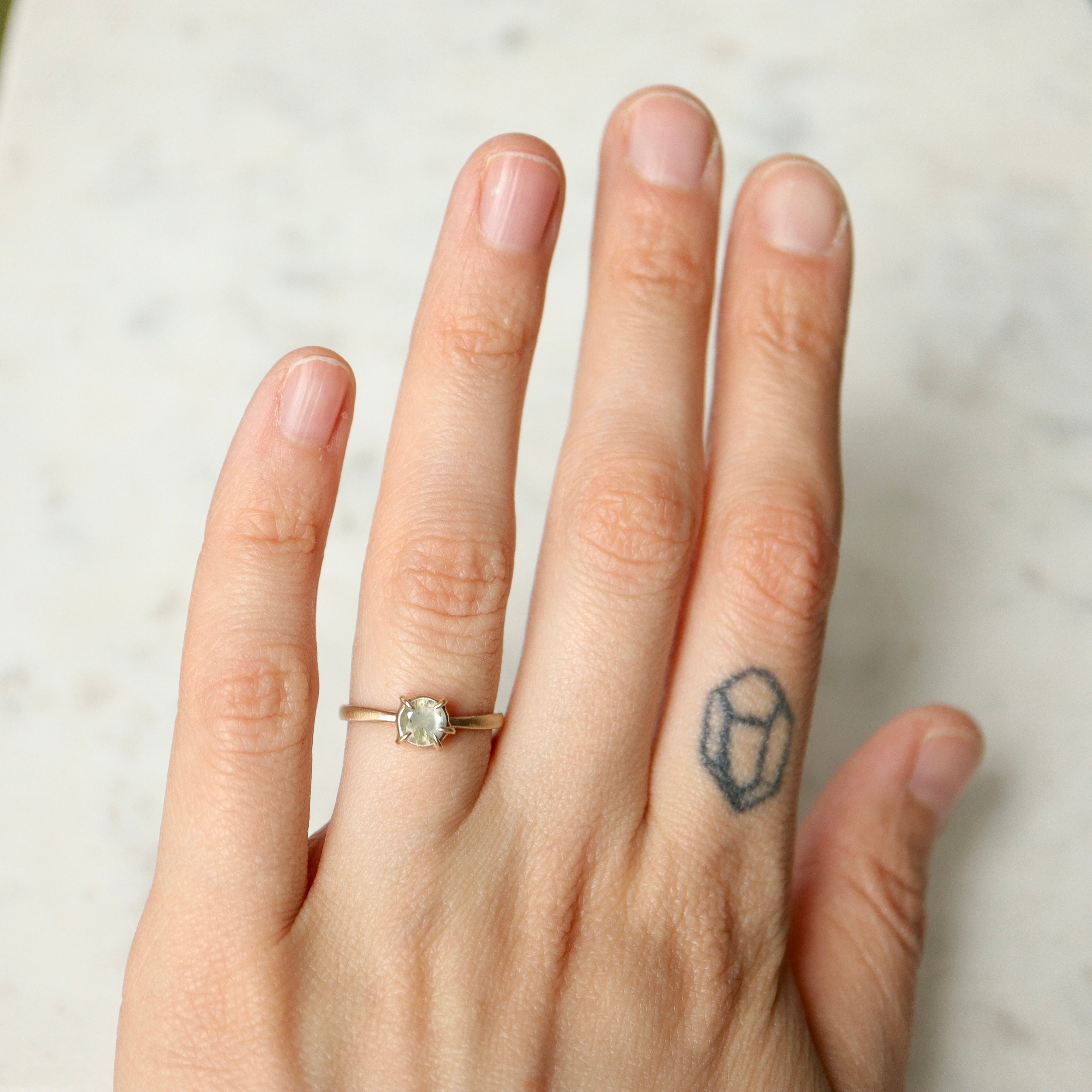 on person view of round cream montana sapphire set in a ring of prongs in a gold ring