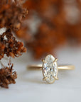 elongated oval diamond set in yellow gold ring with prongs. photographed with brown flowers