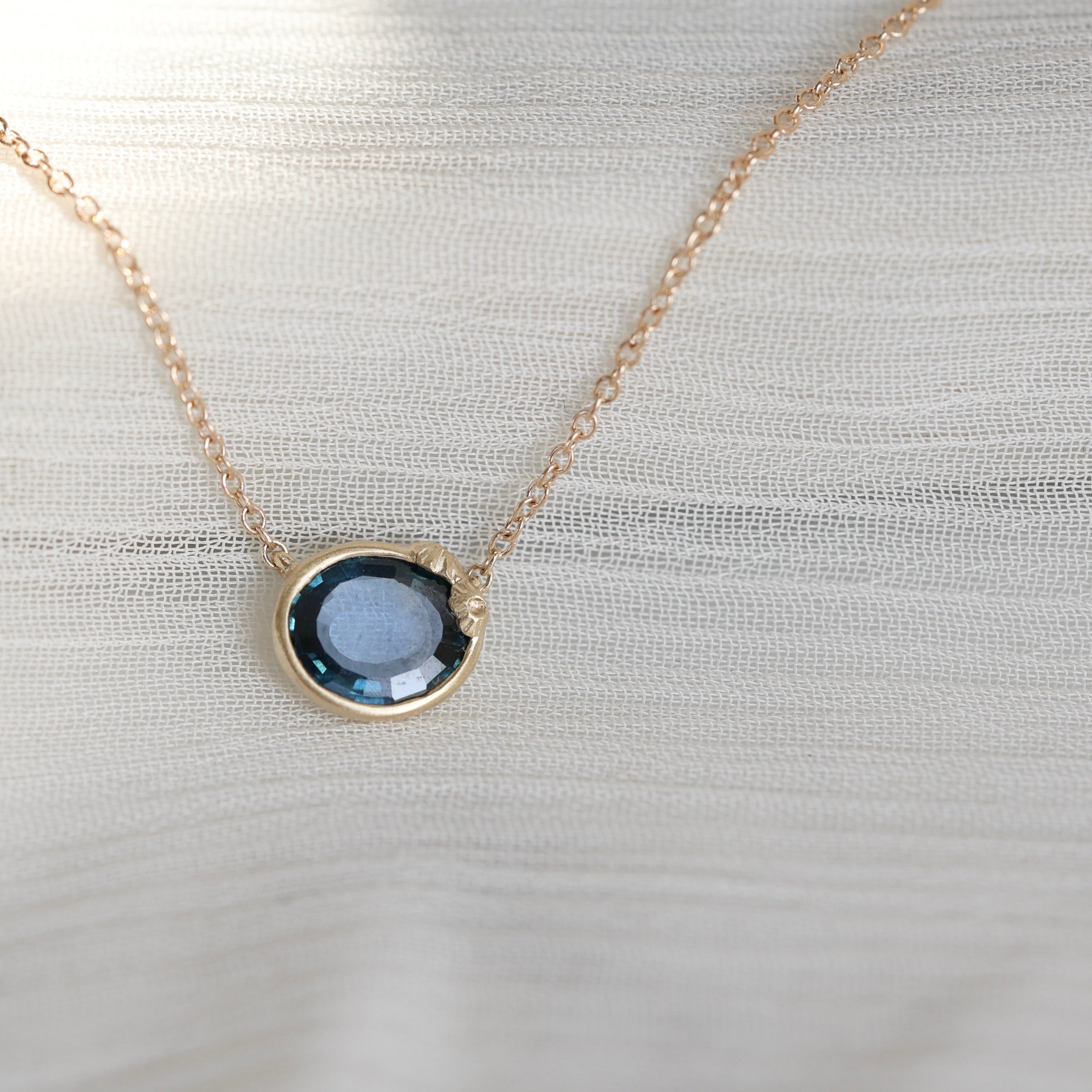 Gold necklace with a blue gemstone pendant on a light fabric background