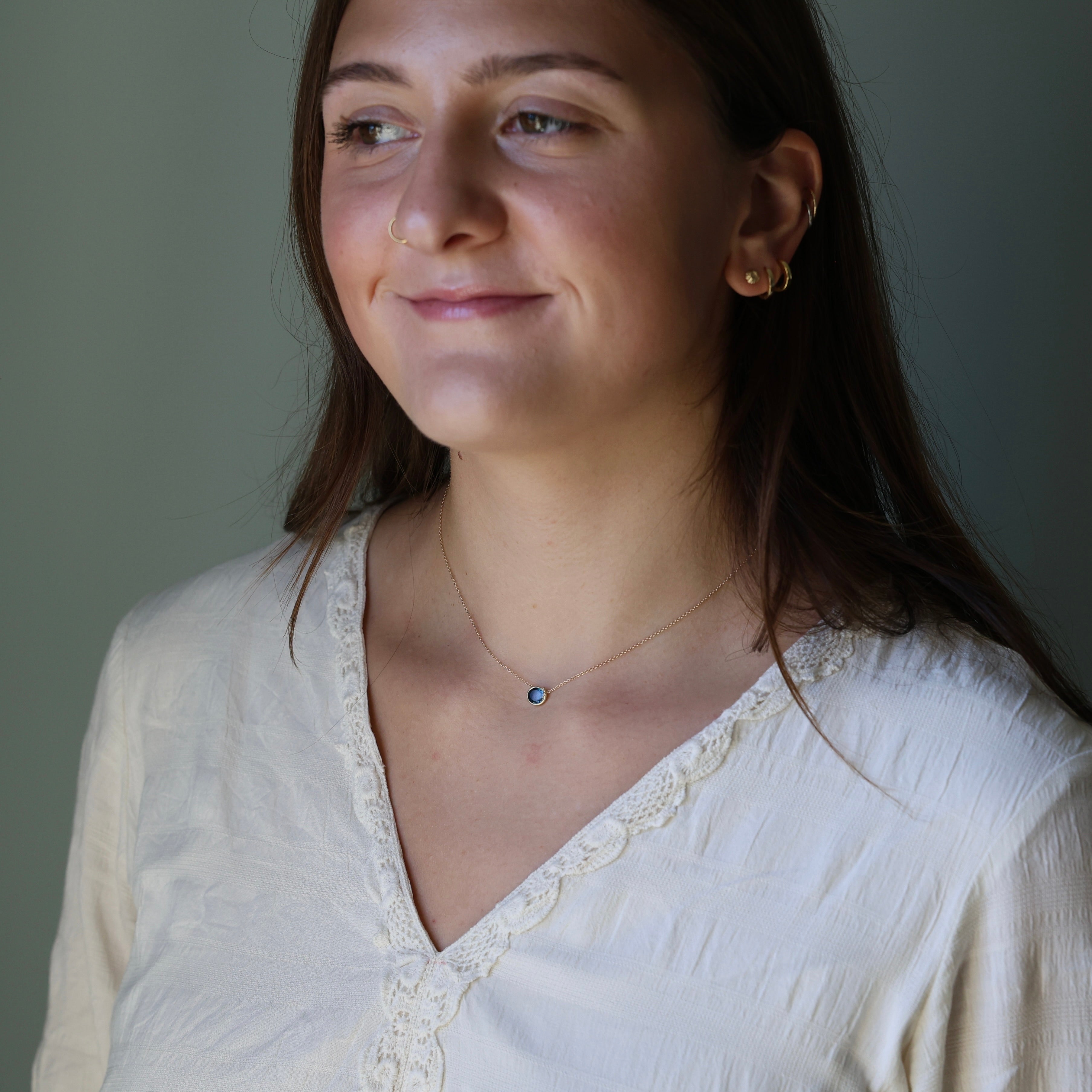 Woman wearing a white blouse with a necklace against a neutral background