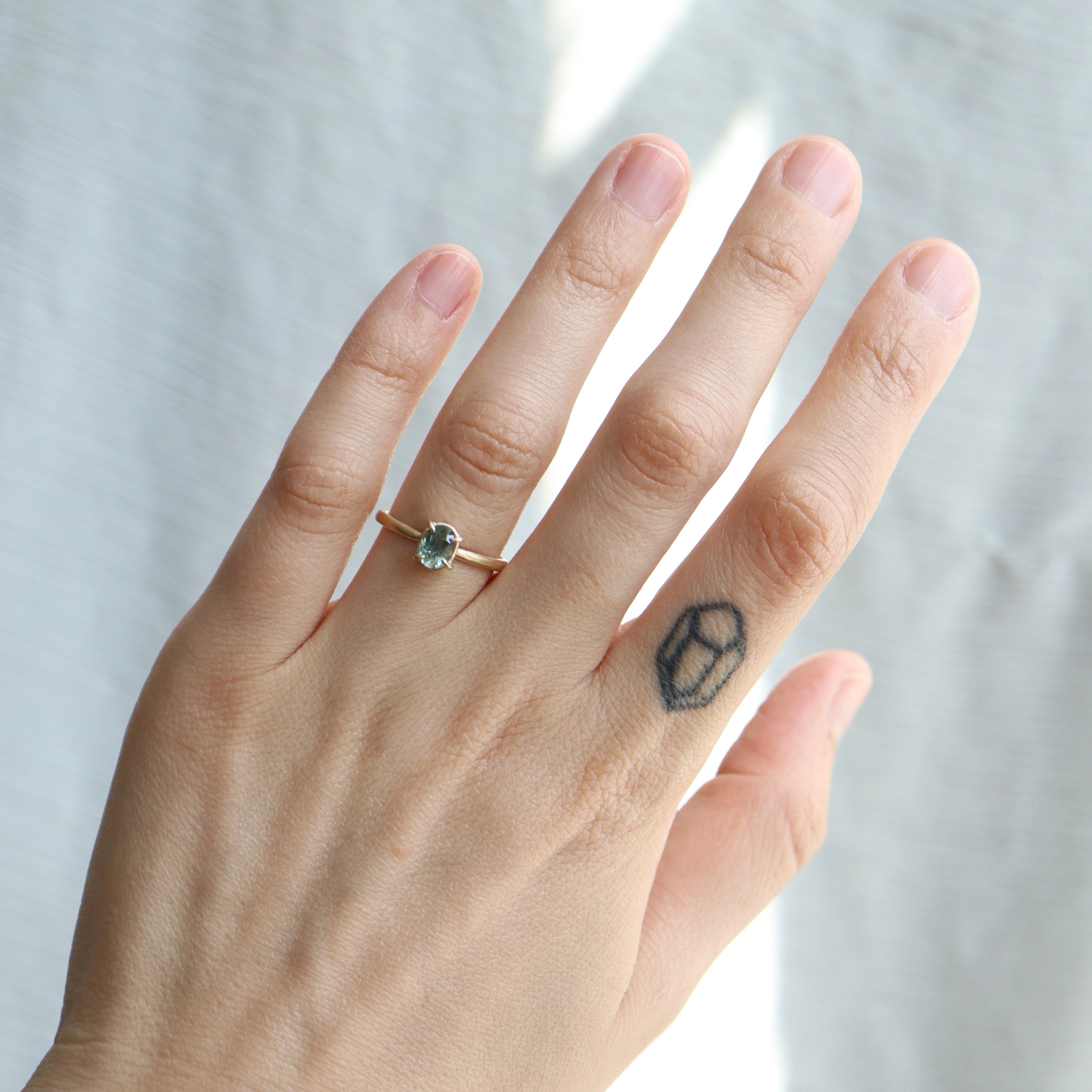 0.83ct Montana sapphire Vanity ring. The pale teal stone is set in 14k yellow gold with four prongs, displayed on a hand. 