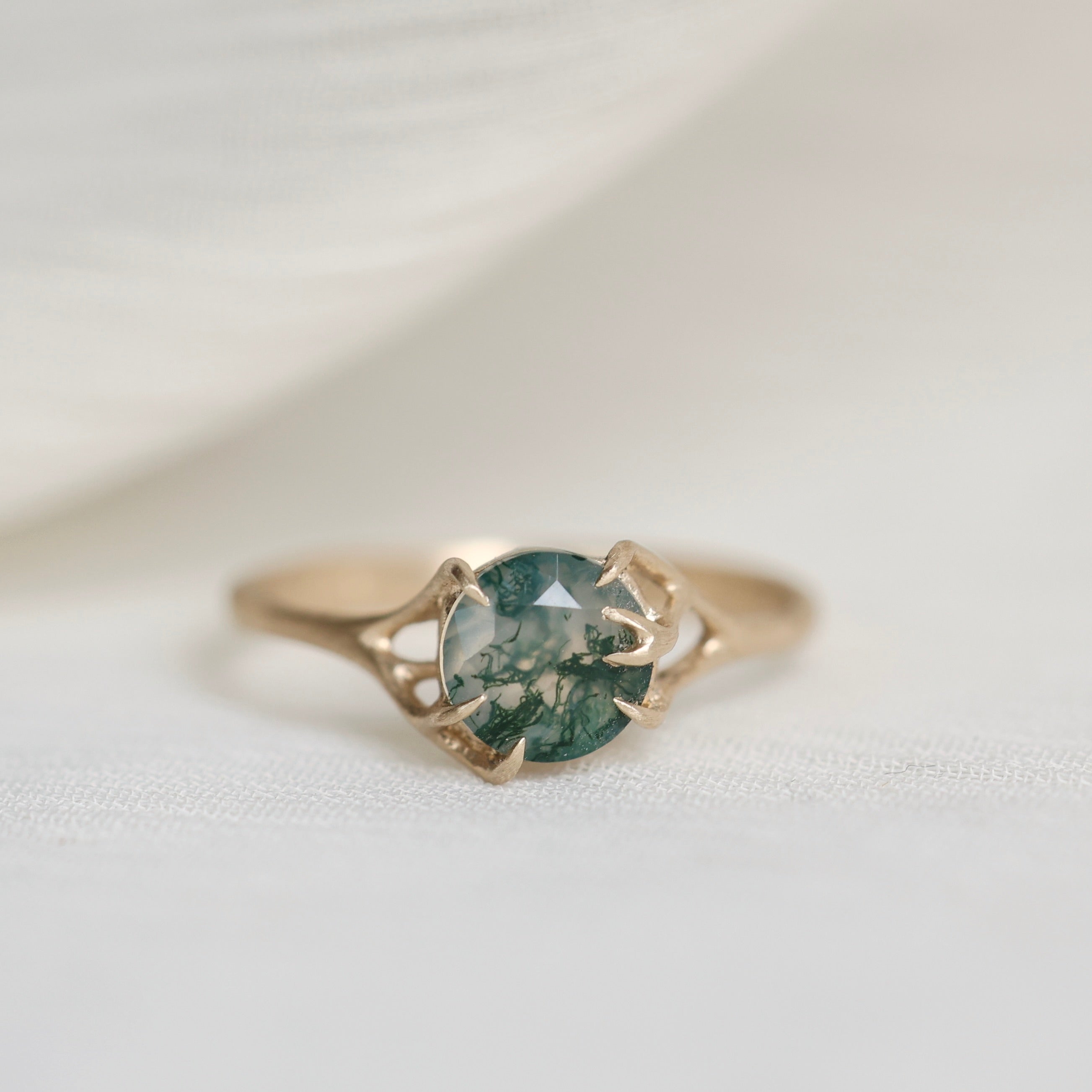 Gold ring with a green gemstone on a white fabric background