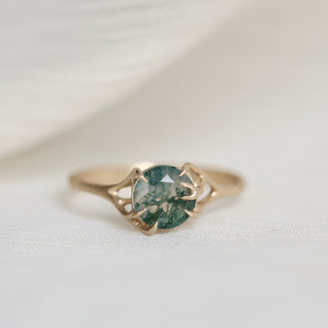 Gold ring with a green gemstone on a white fabric background