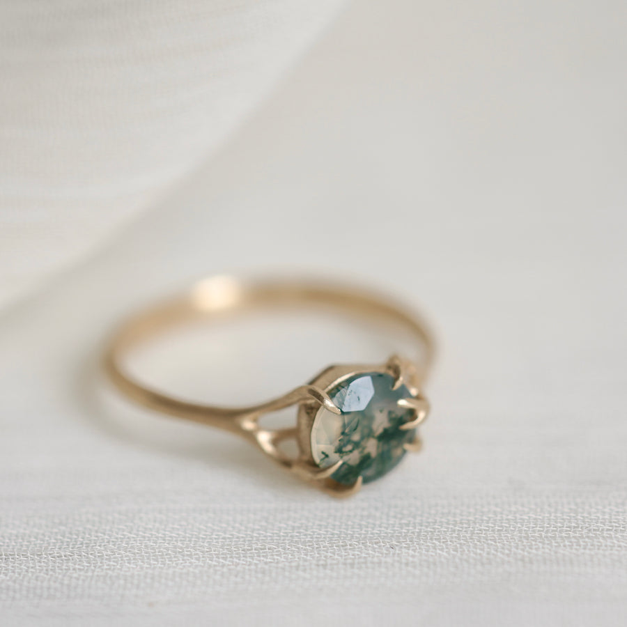Gold ring with a green gemstone on a light fabric background