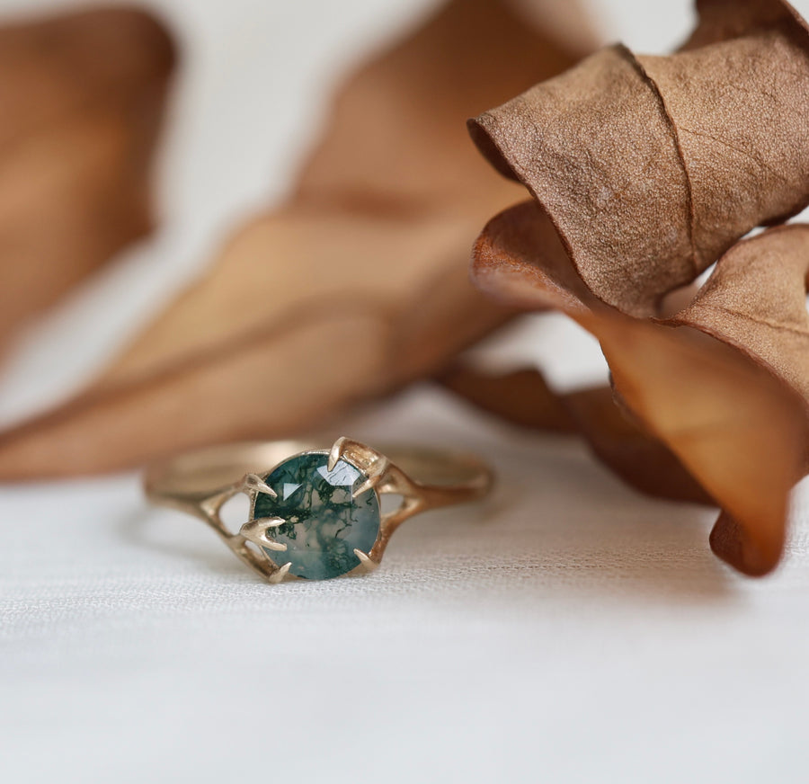 Gold ring with a green gemstone on a white surface with brown leaves.