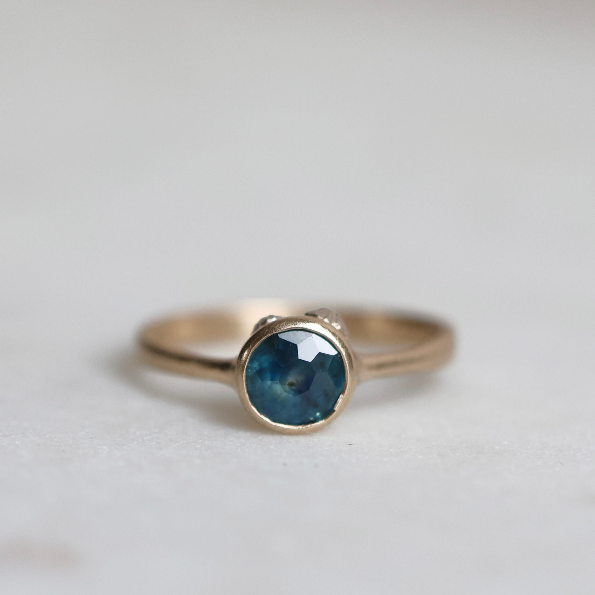 Gold ring with a blue sapphire on a light gray background