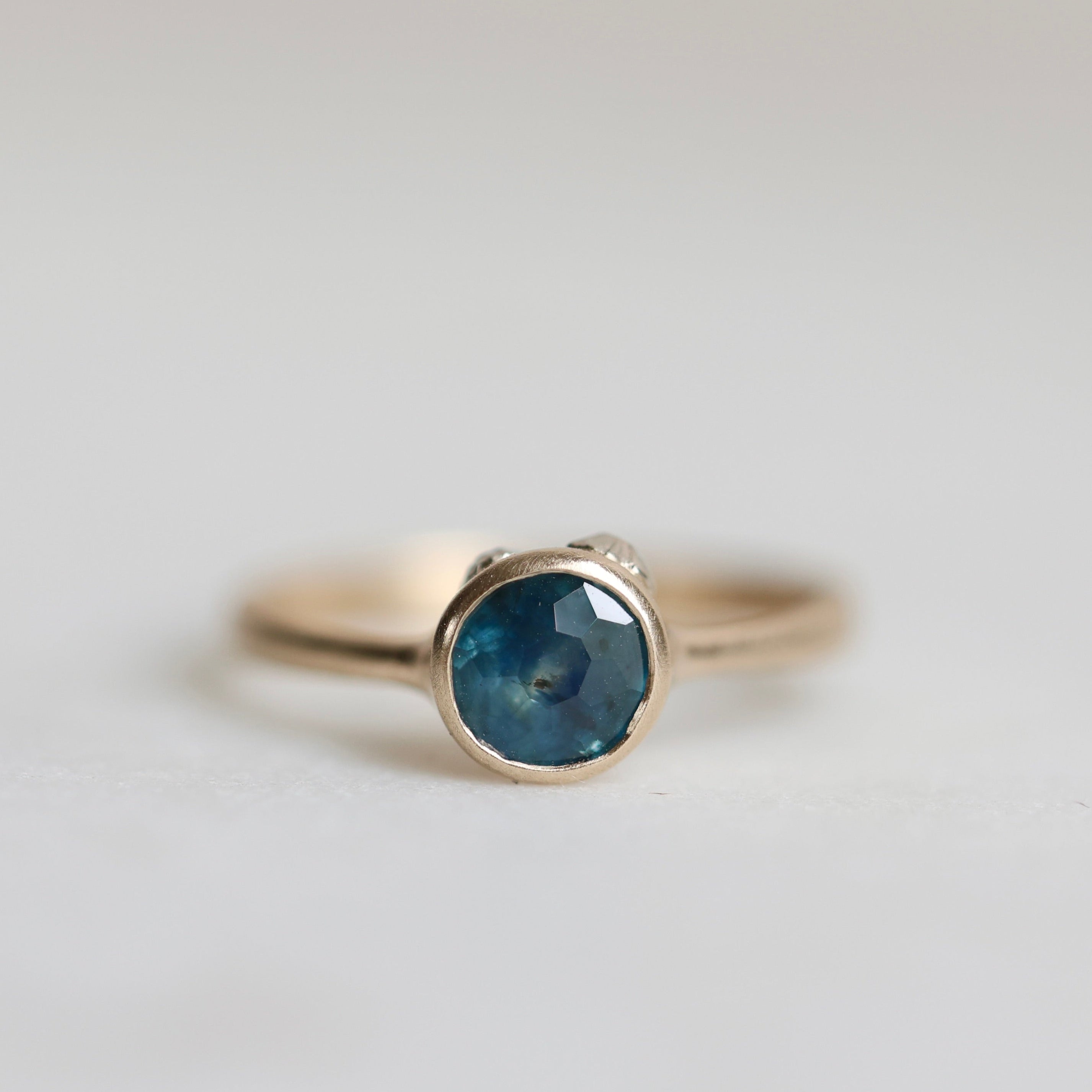Gold ring with a blue gemstone on a light gray background