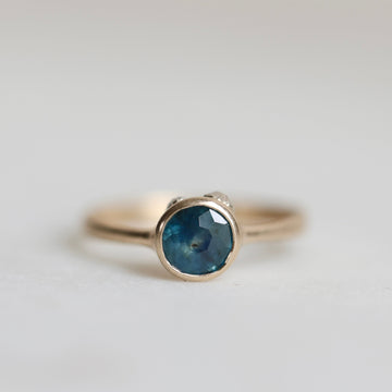 Gold ring with a blue gemstone on a light gray background