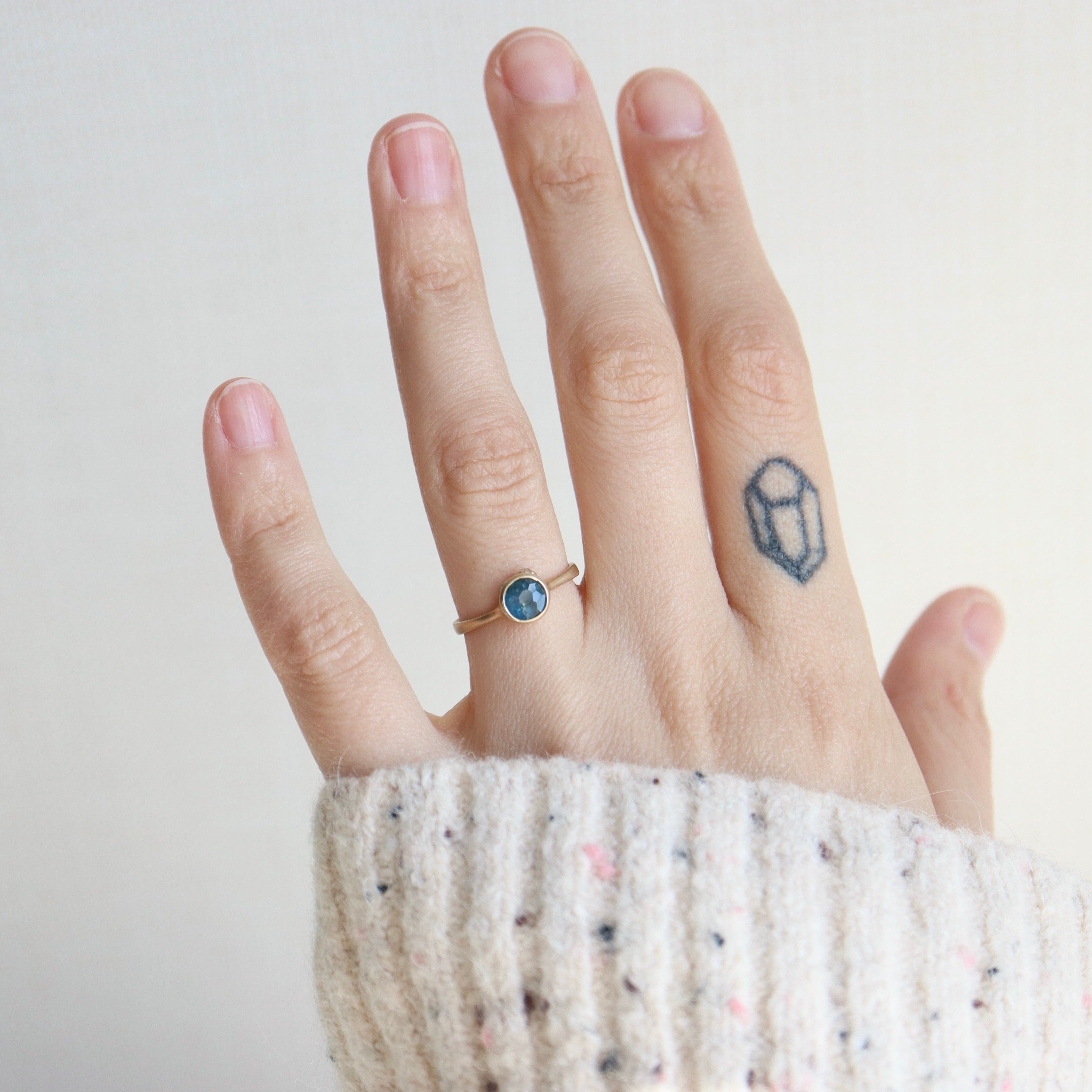 Hand wearing a ring with a small tattoo on the finger against a plain background