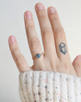 Hand wearing a ring with a small tattoo on the finger against a plain background