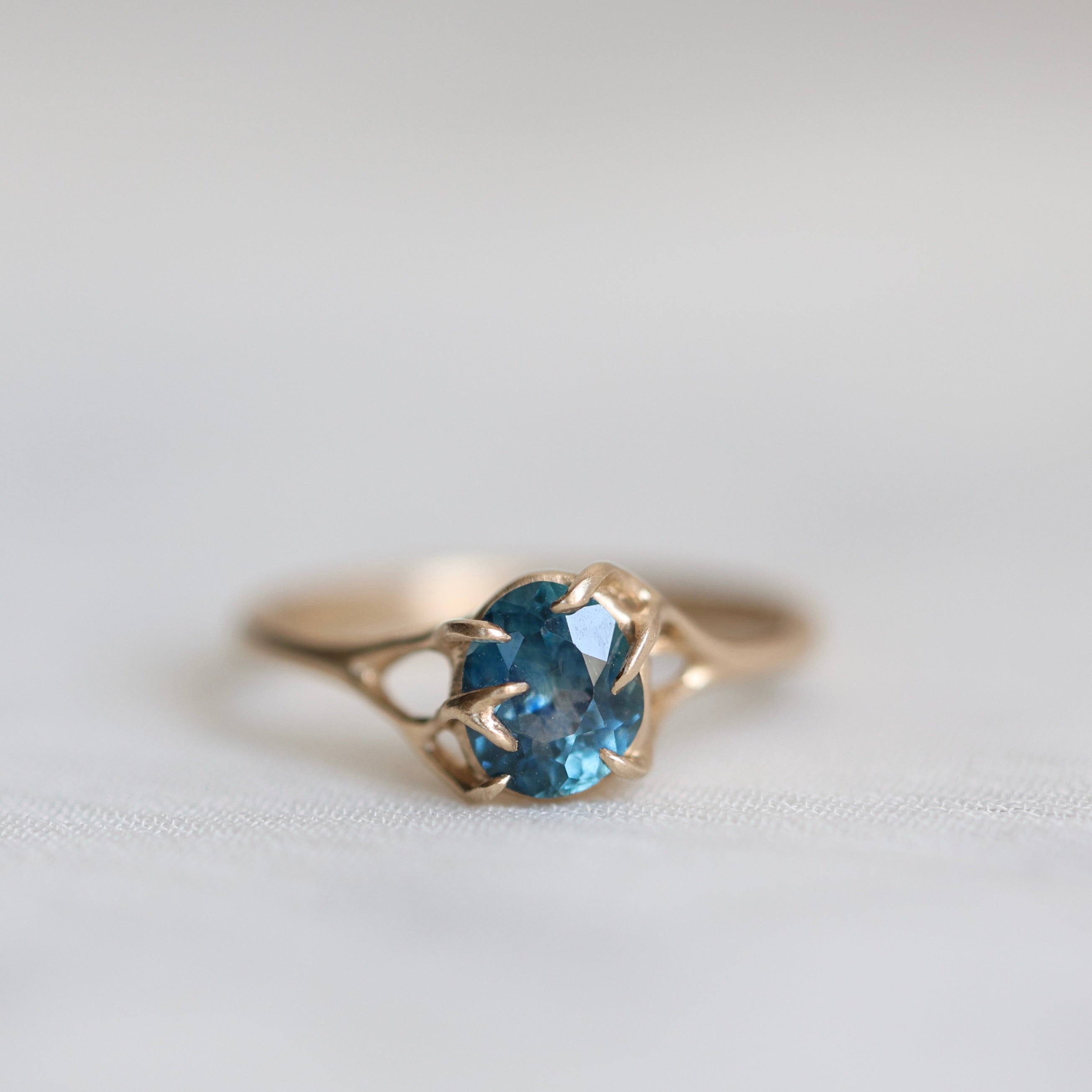 Gold ring with a blue gemstone on a light gray background