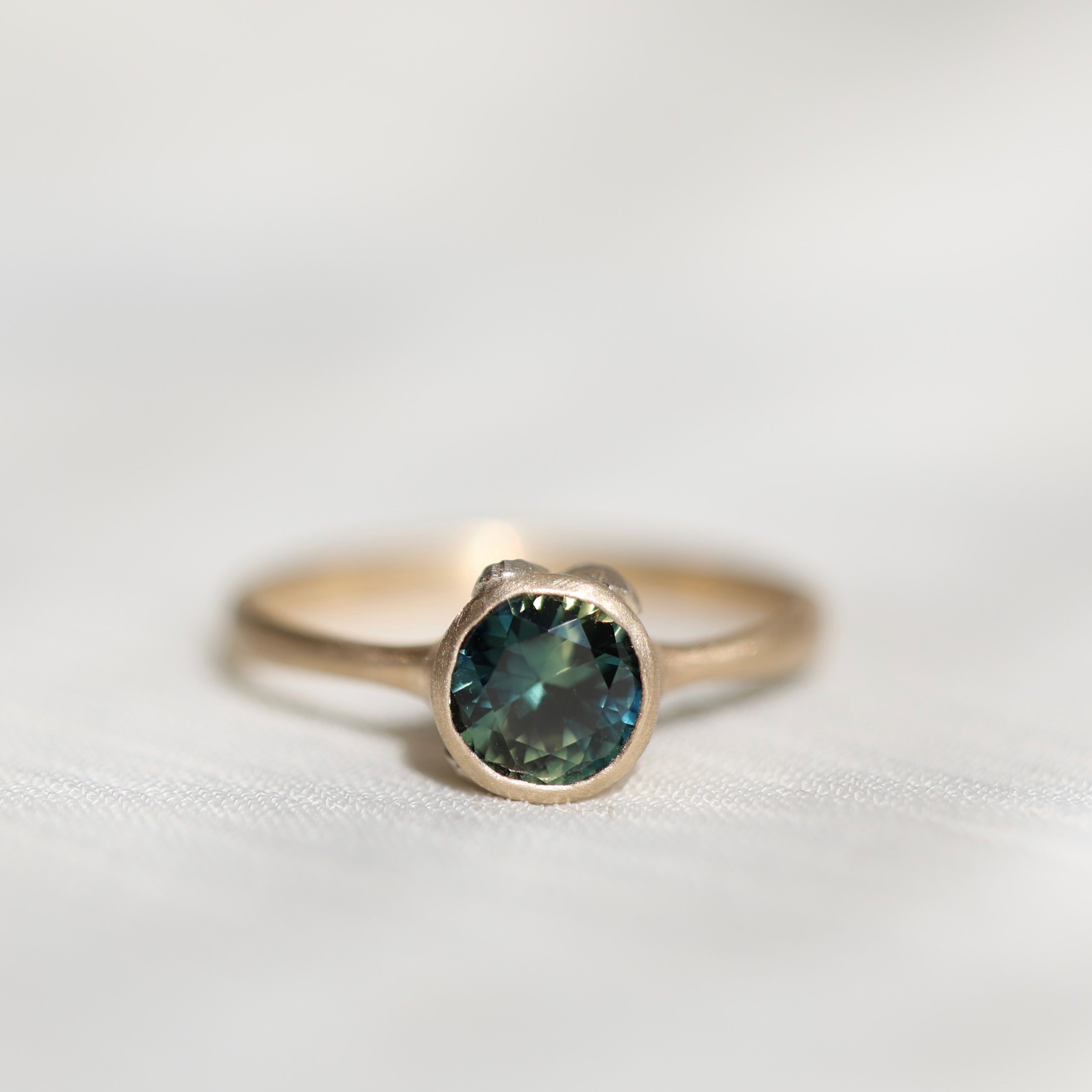 Gold ring with a teal gemstone on a light gray background
