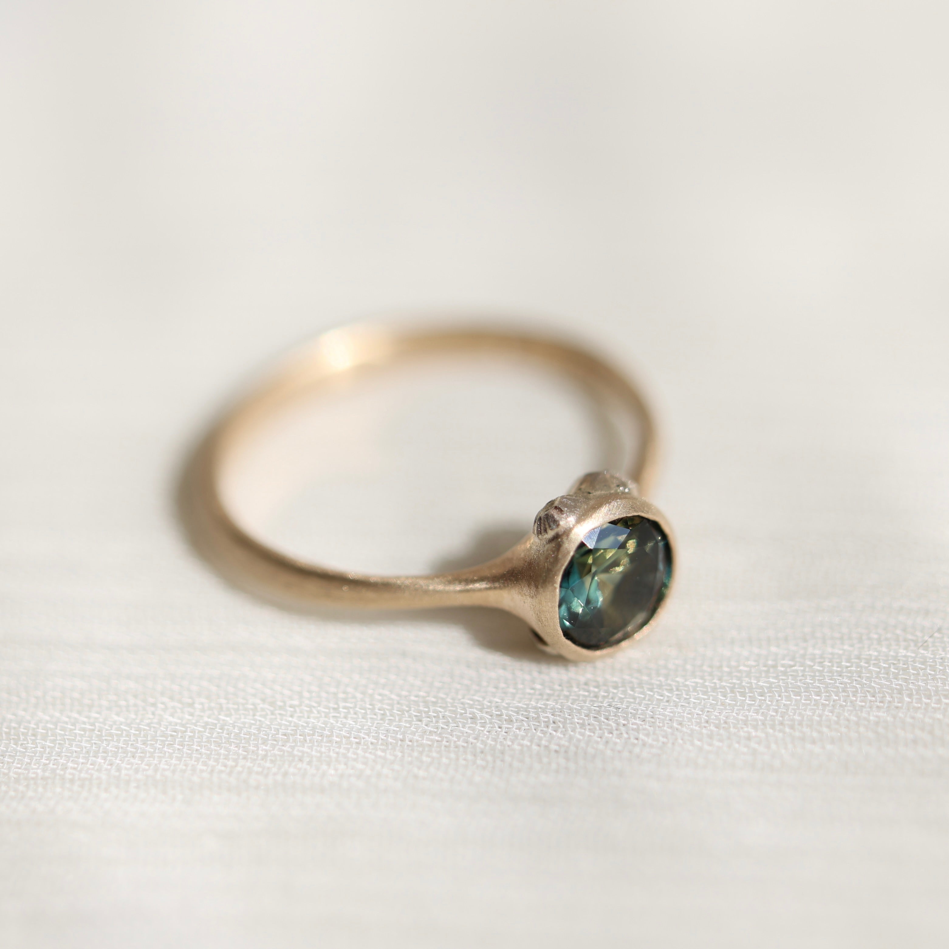 Gold ring with a teal gemstone on a white fabric background