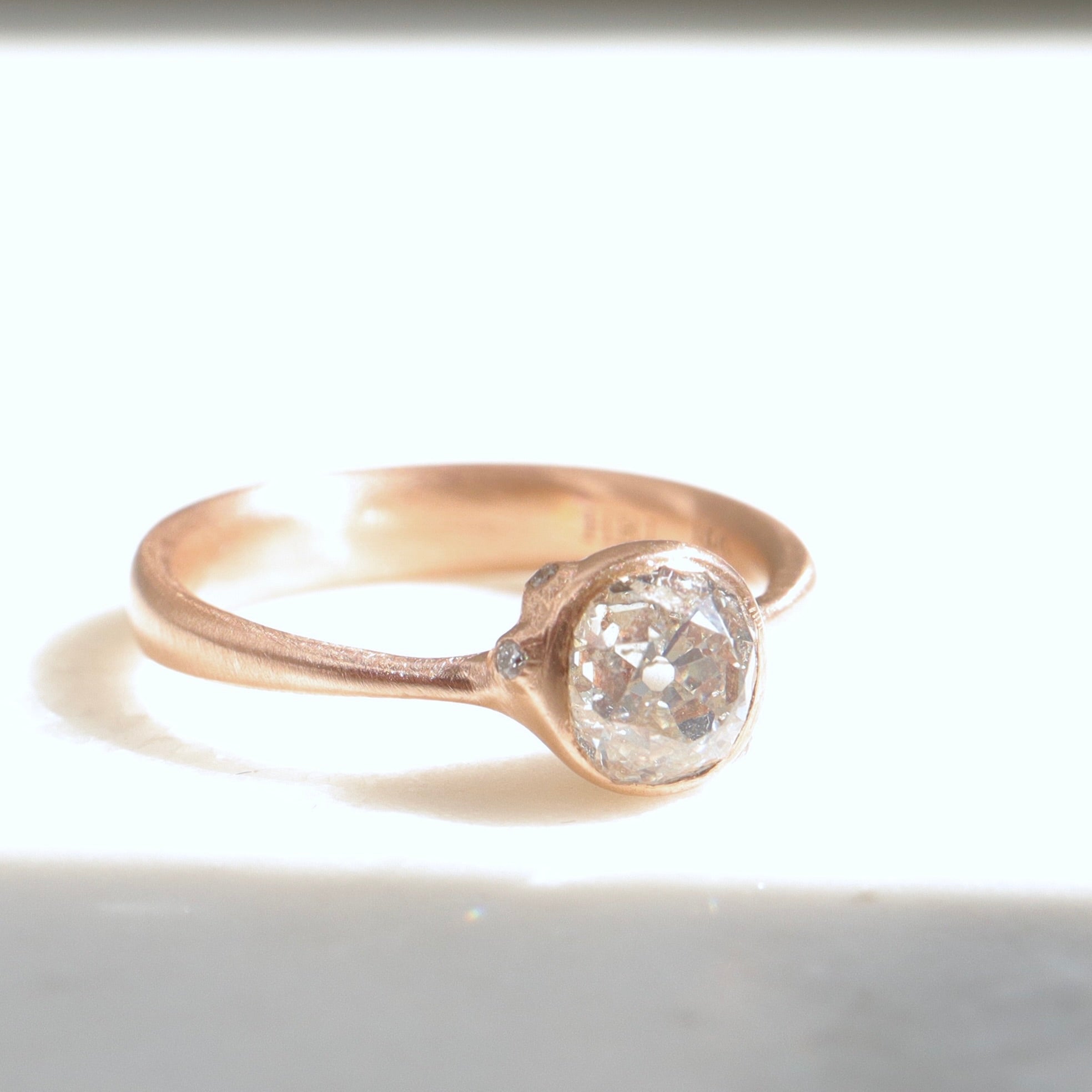 rose gold ring with diamond and three small side barnacles with diamonds- 1/4 view, in light.