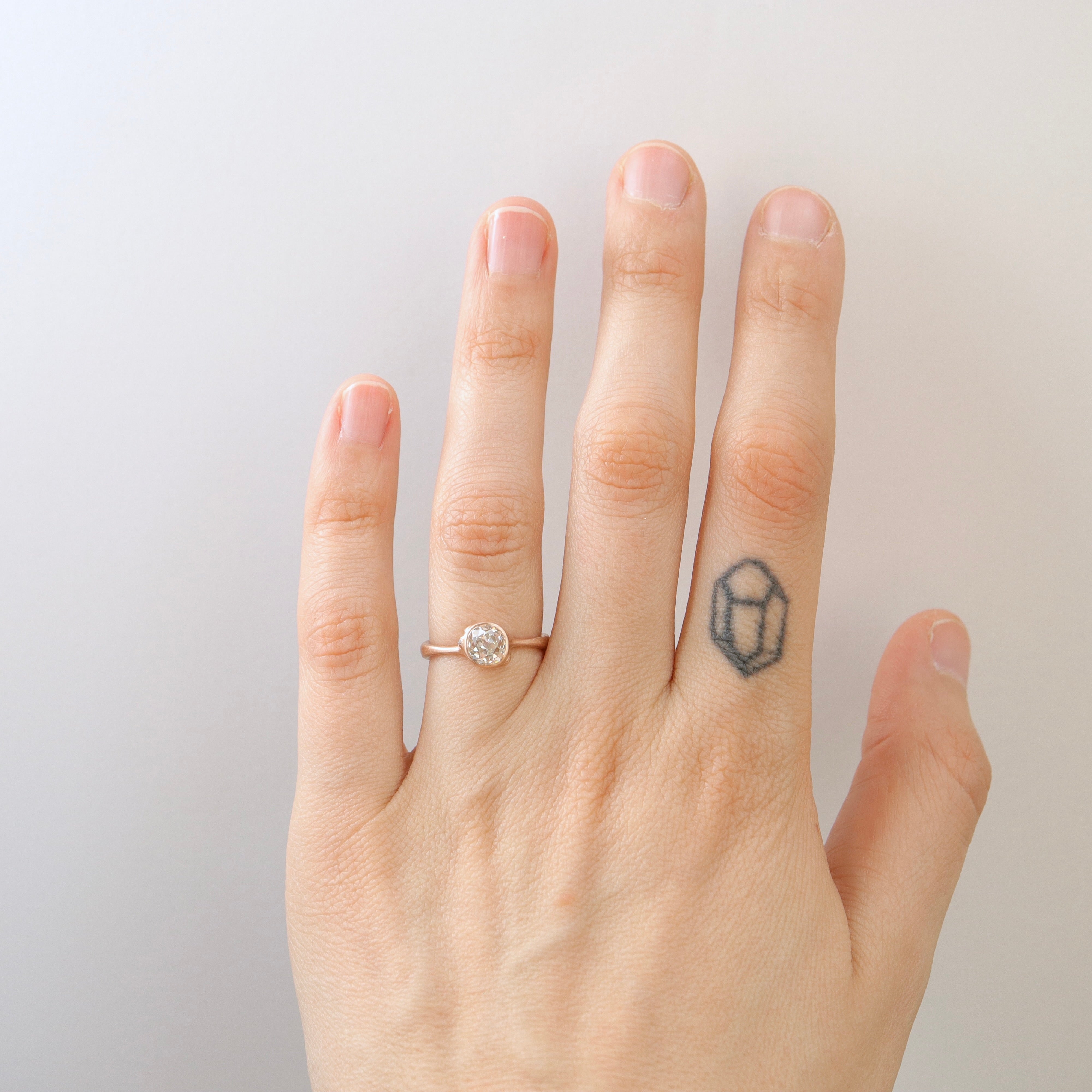 rose gold ring with diamond and three small side barnacles with diamonds- shown on hand.