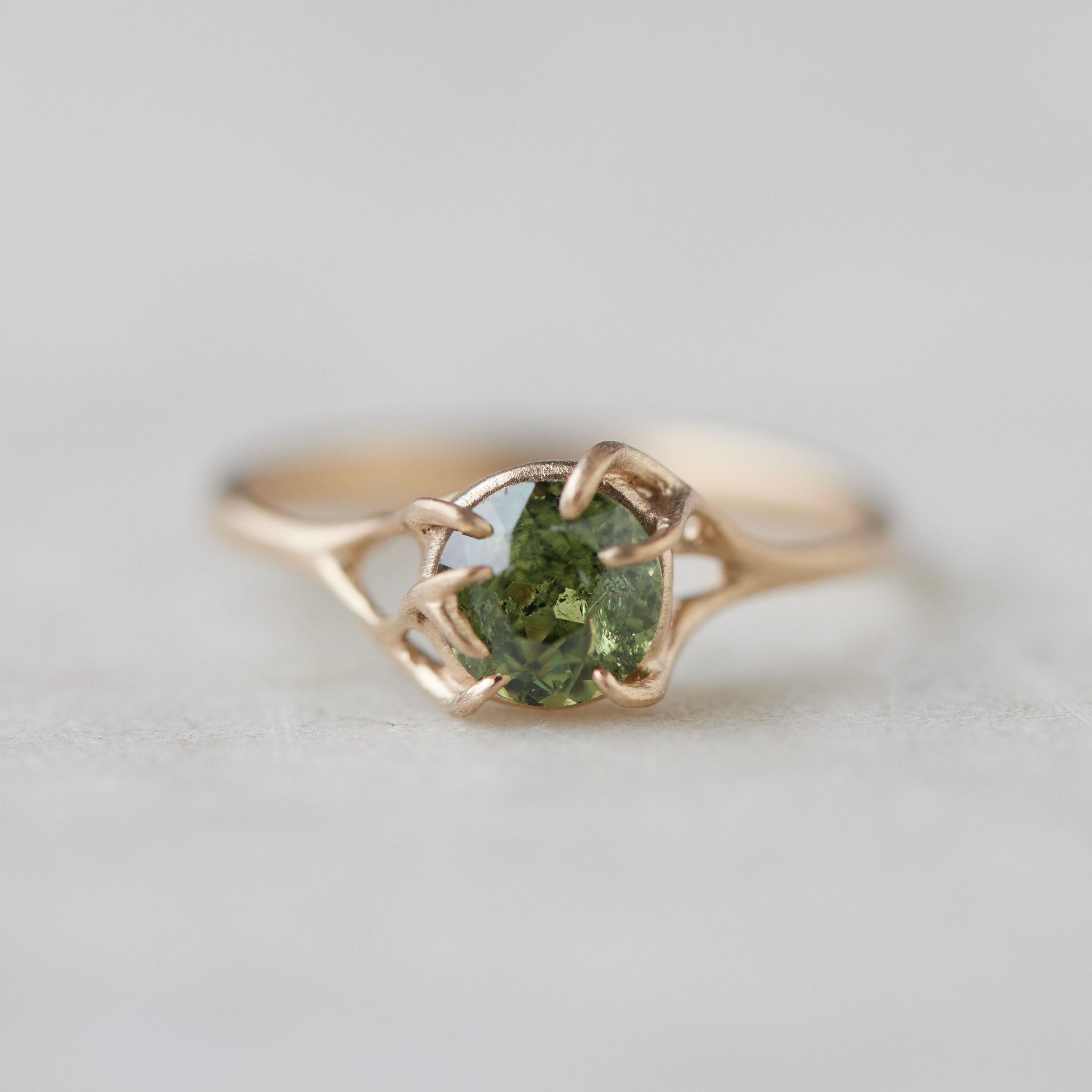 a heavily included green garnet round gemstone is set in a gold branch ring with vine-like prongs. Front view.