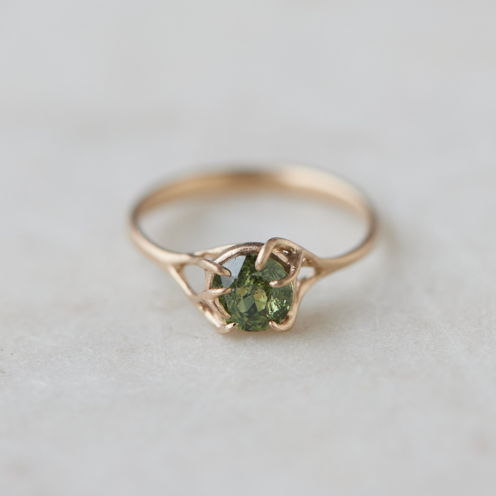 a heavily included green garnet round gemstone is set in a gold branch ring with vine-like prongs. Front view.