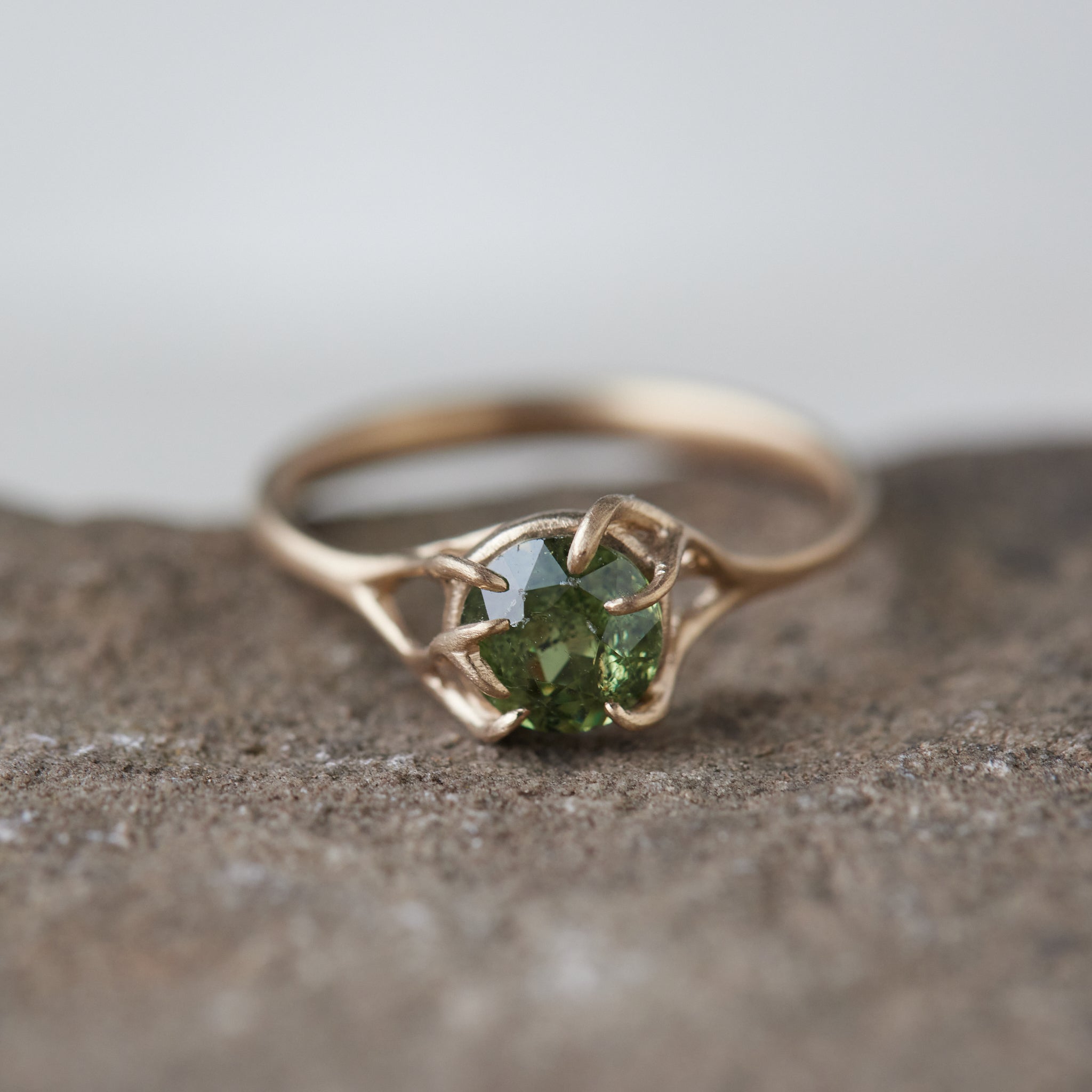 a heavily included green garnet round gemstone is set in a gold branch ring with vine-like prongs. Front view.