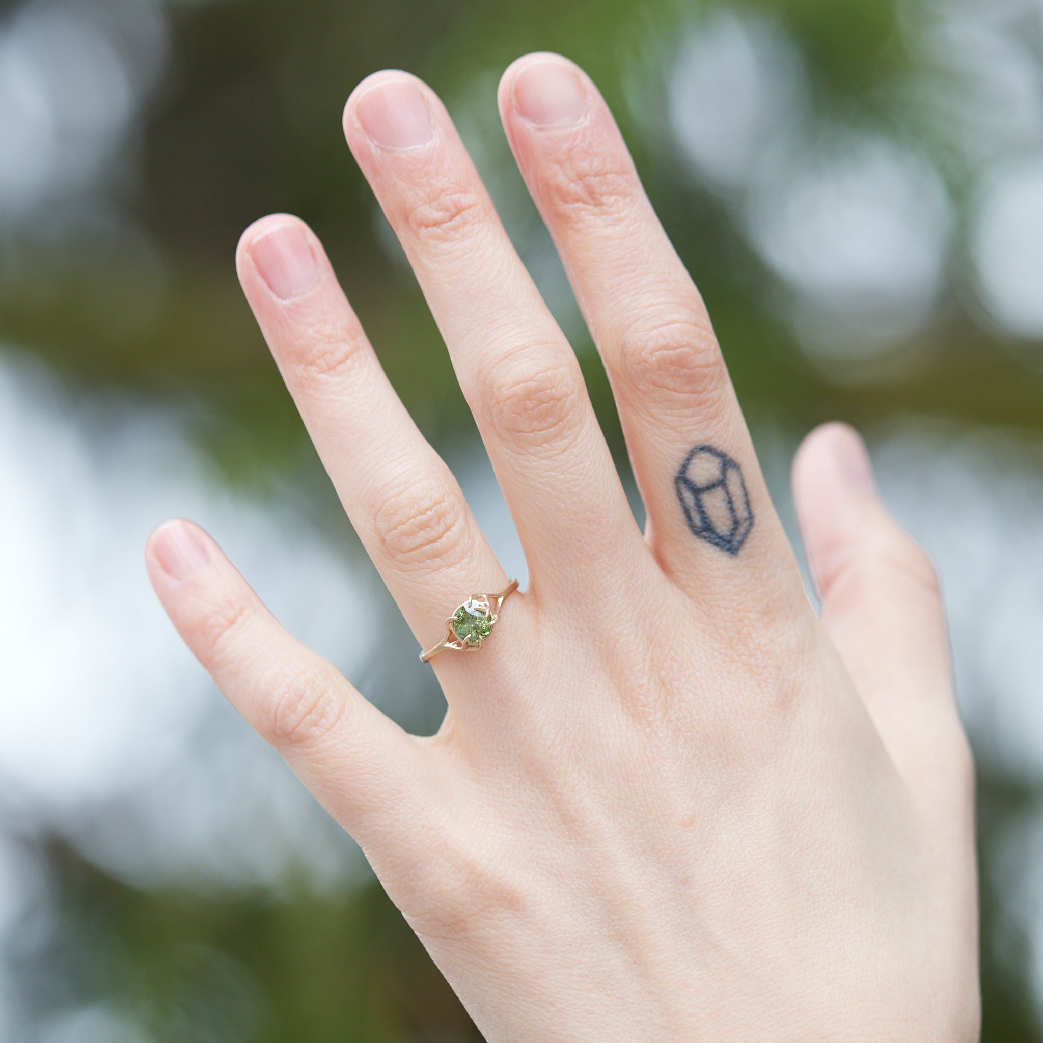 a heavily included green garnet round gemstone is set in a gold branch ring with vine-like prongs. Shown on person.