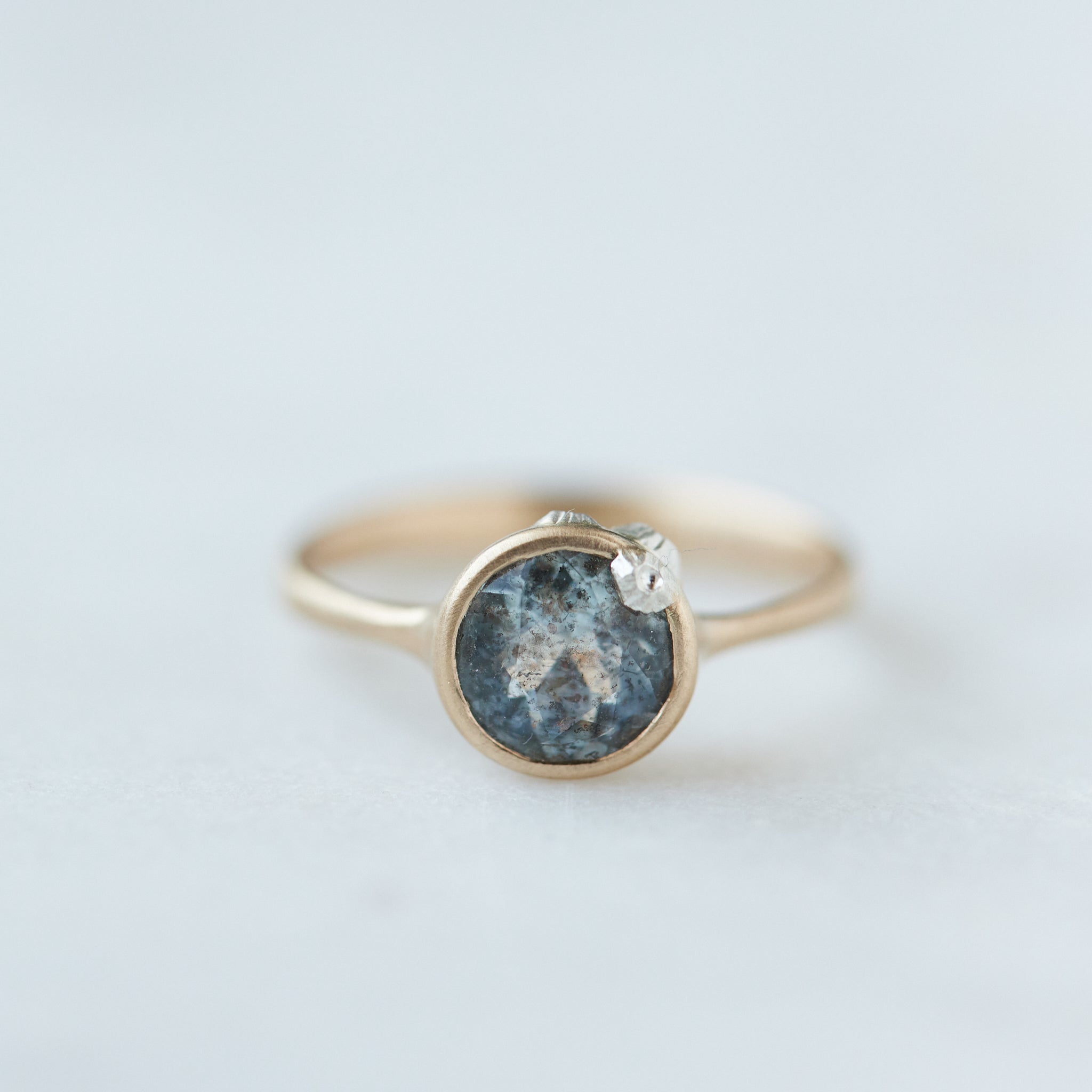 round aquamarine with black speckles set in gold bezel ring with silver barnacles. Front view.
