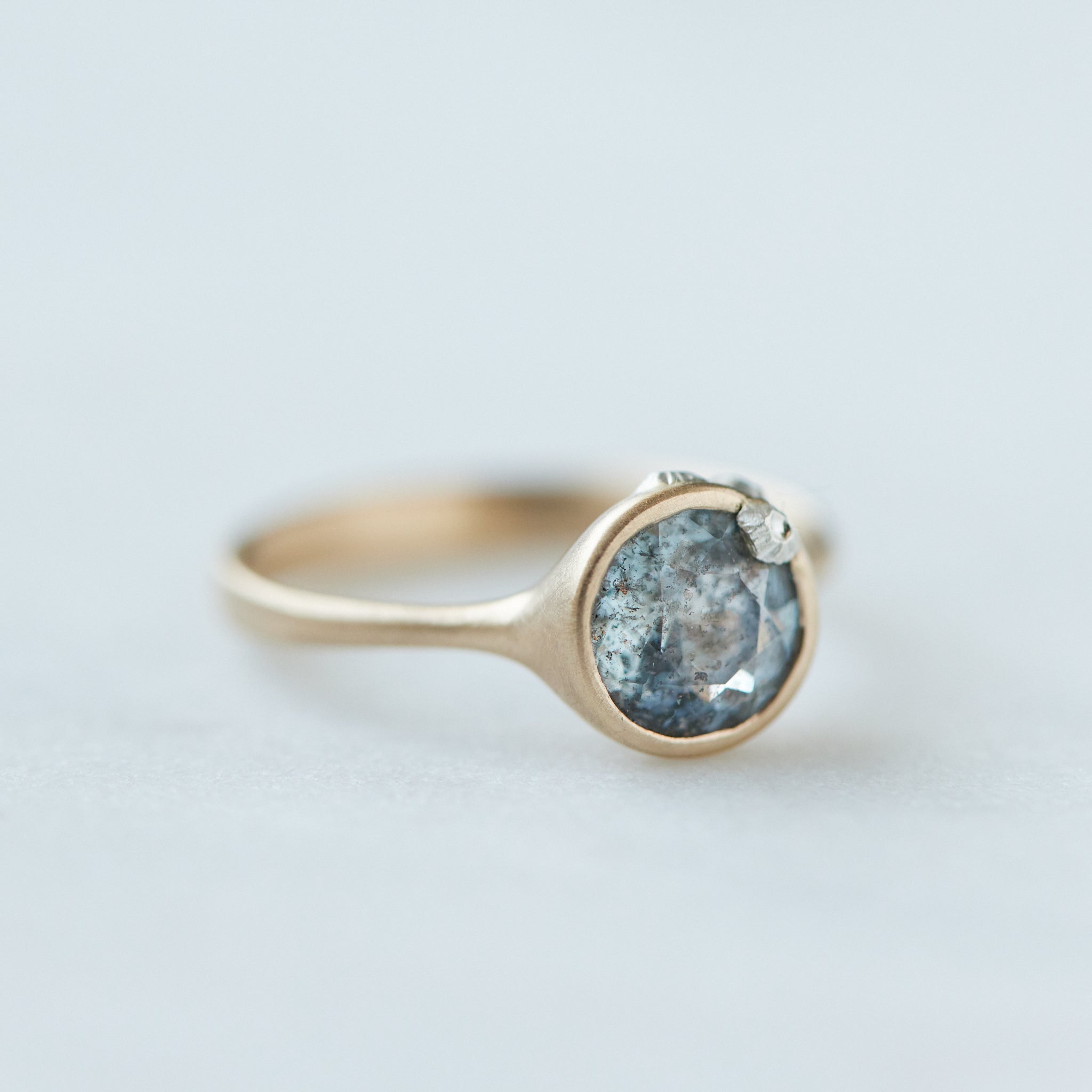 round aquamarine with black speckles set in gold bezel ring with silver barnacles. Side view.