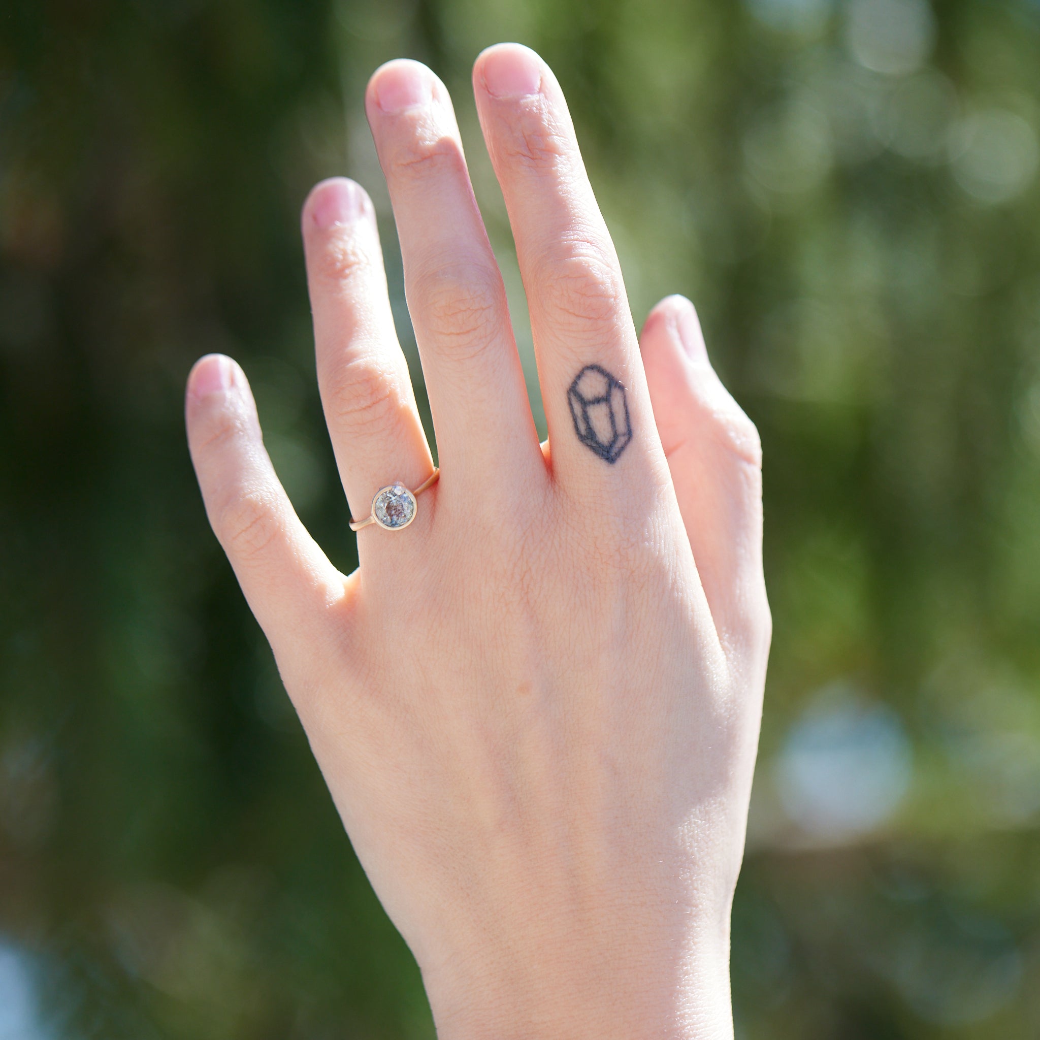 round aquamarine with black speckles set in gold bezel ring with silver barnacles. Photographed on person.