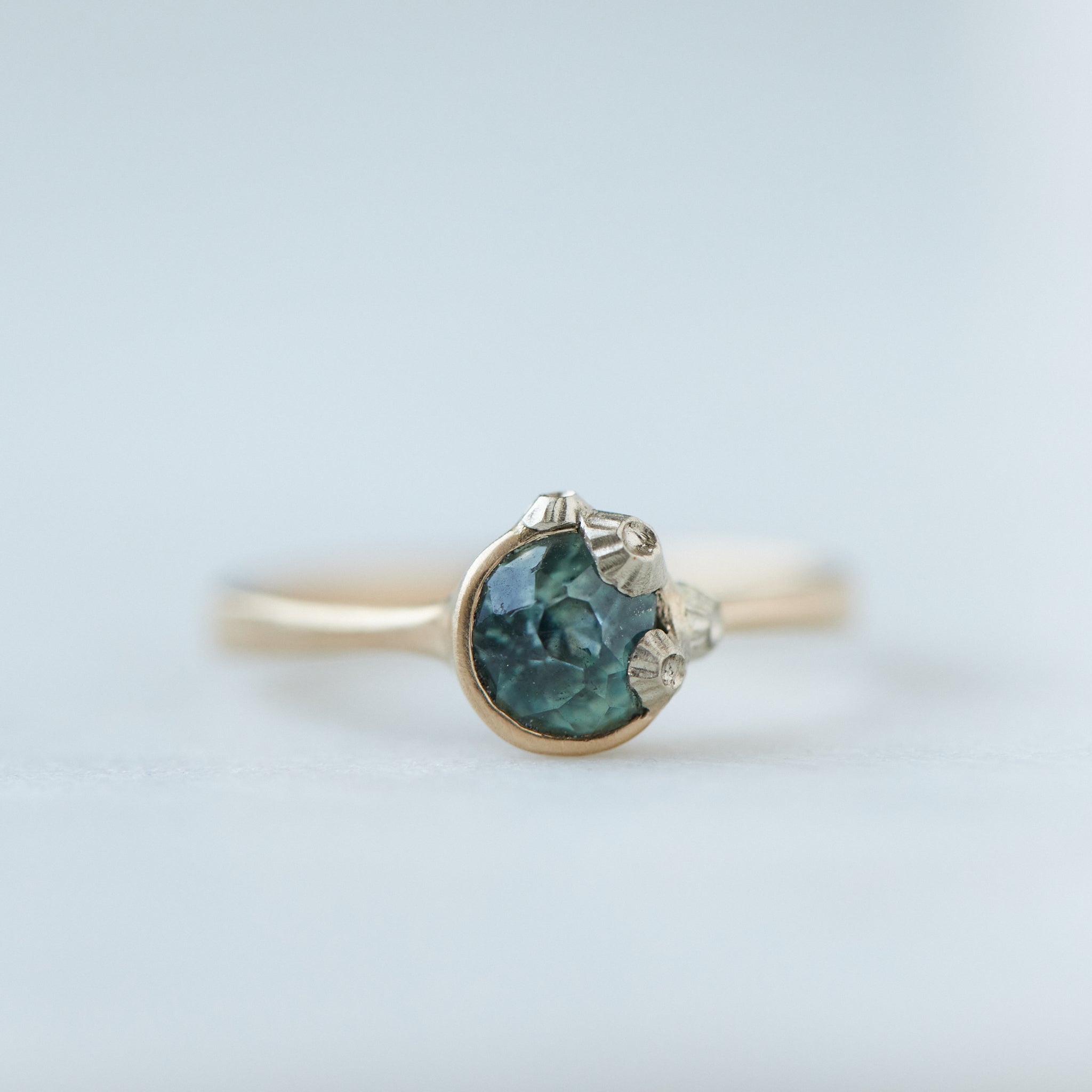 a half moon montana sapphire is set in a gold bezel ring with white gold barnacles. Front view.