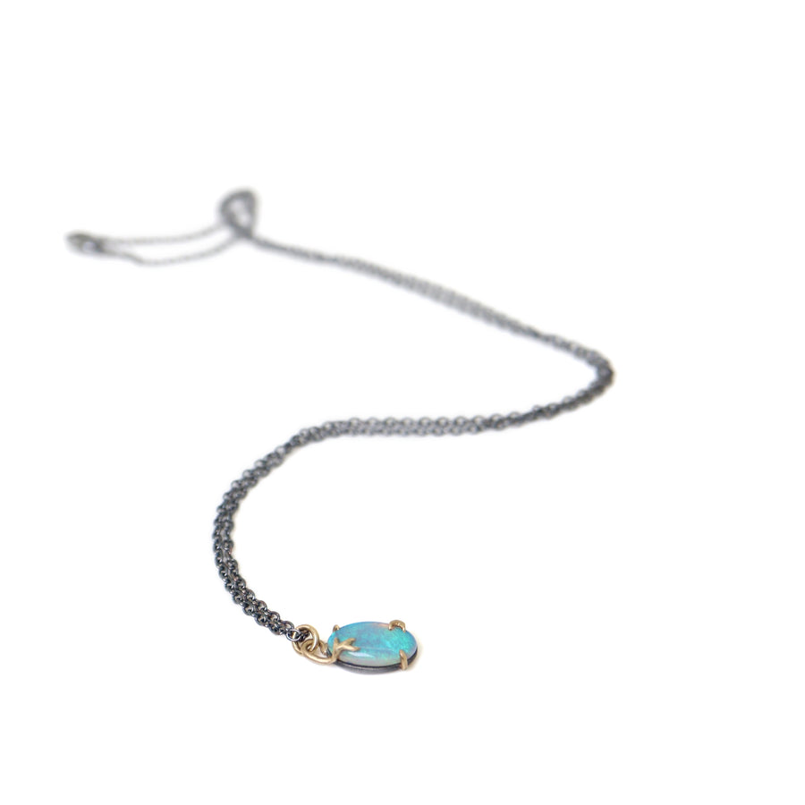 green and blue flash oval opal set in gold branch prongs, on a black chain, on white. by hannah blount