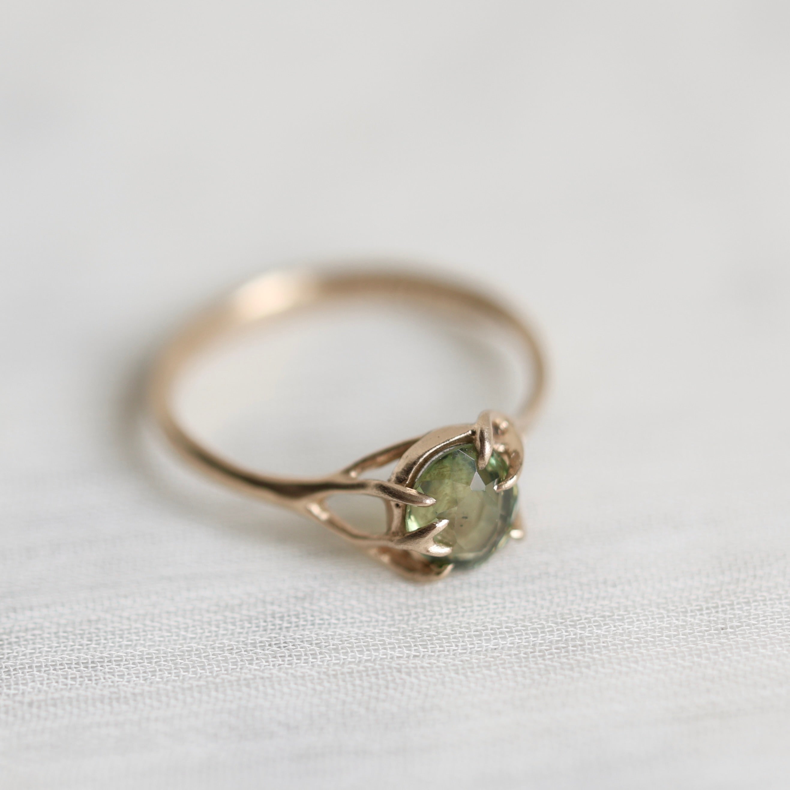 Gold ring with a green gemstone on a light fabric background