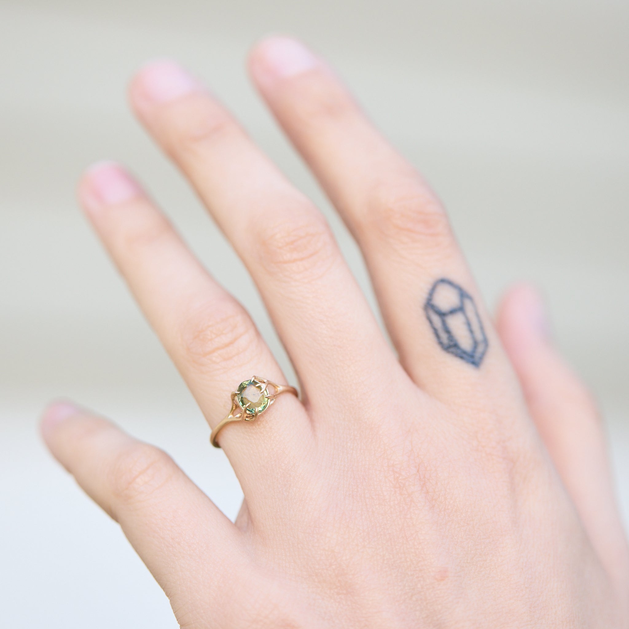 Hand wearing a gold ring with a green gemstone on a plain background