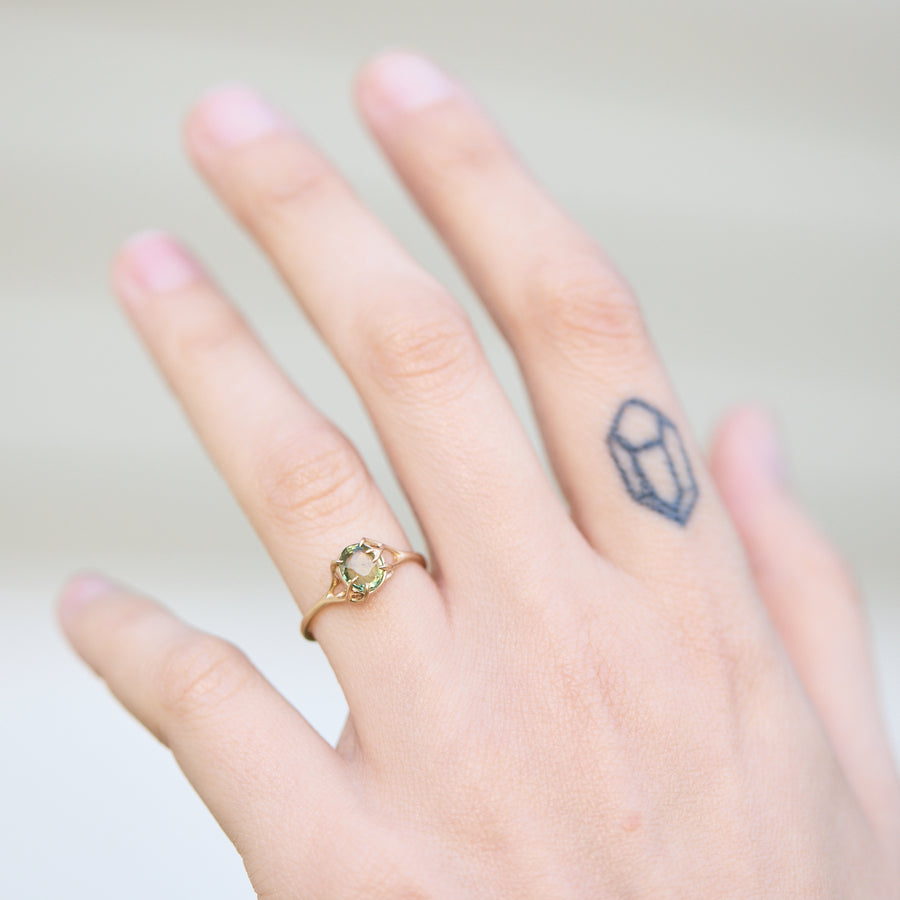 Hand wearing a gold ring with a green gemstone on a plain background