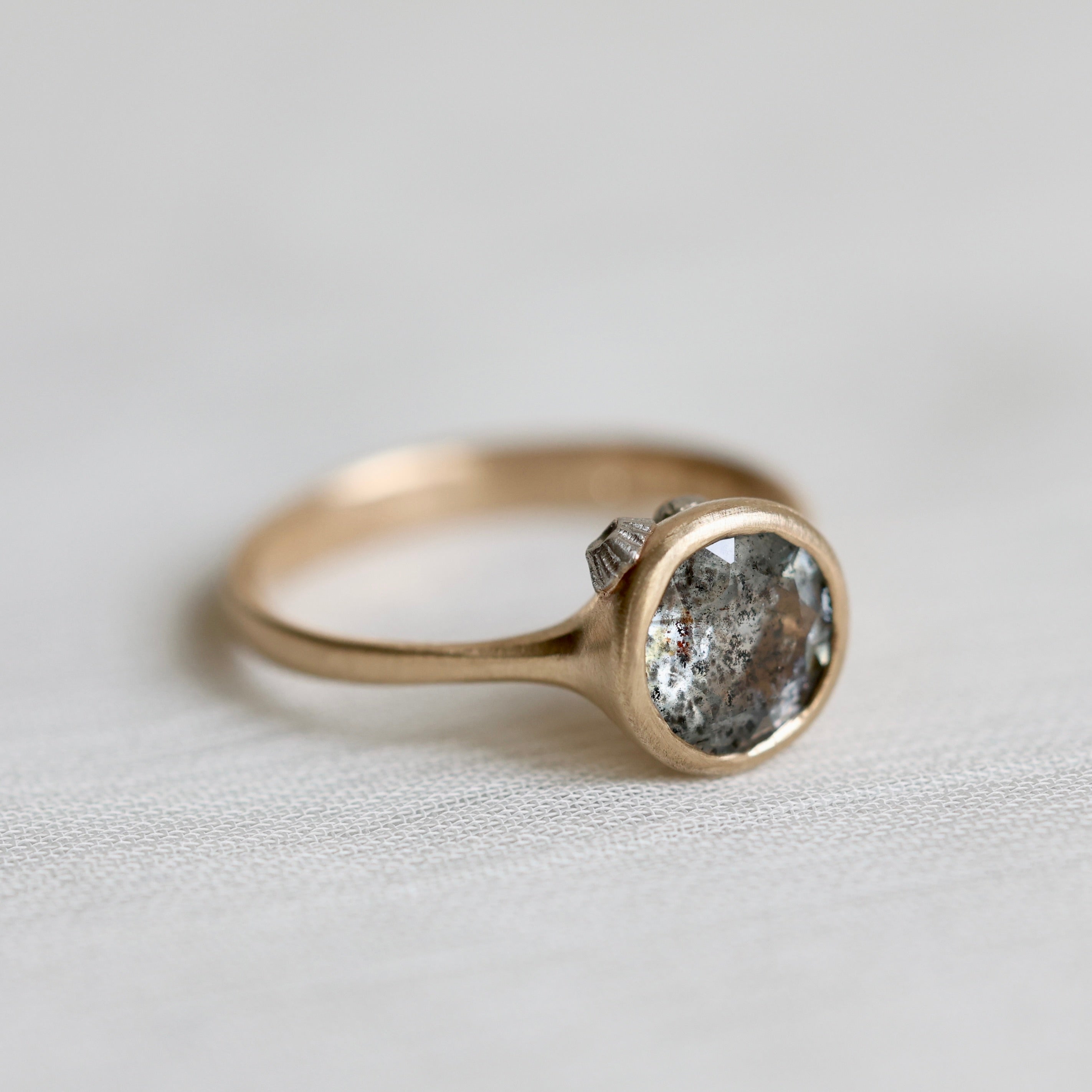 Gold ring with a textured gemstone on a light gray background