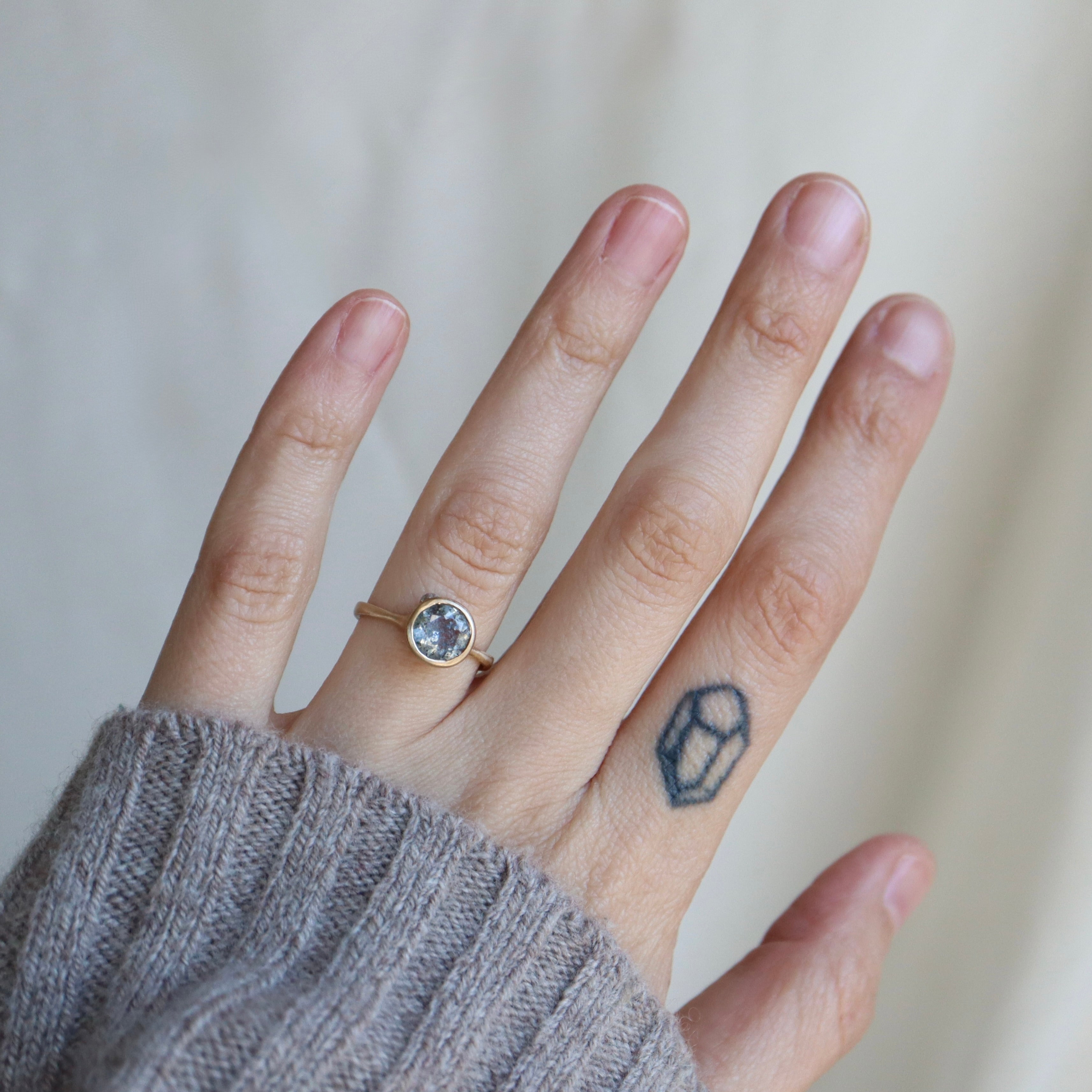 Hand wearing a ring with a small gemstone on a neutral background
