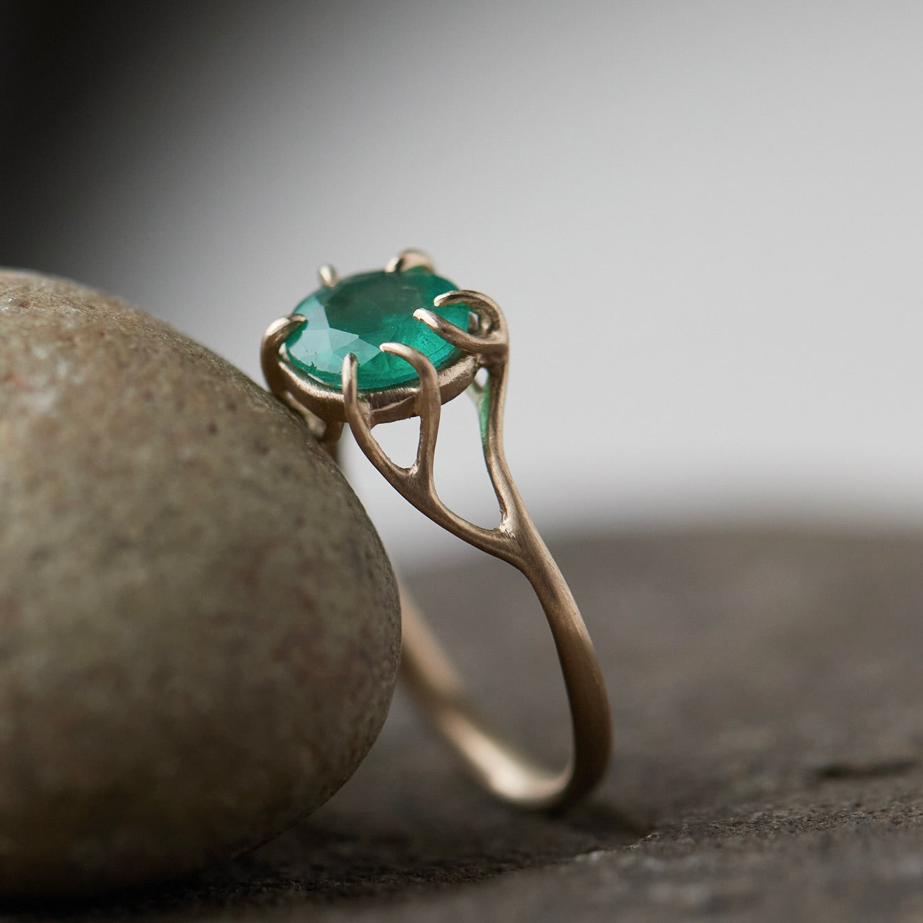 Round green emerald is set in a branch ring with branchy prongs holding the stone. Photographed leaving on a stone. side view.
