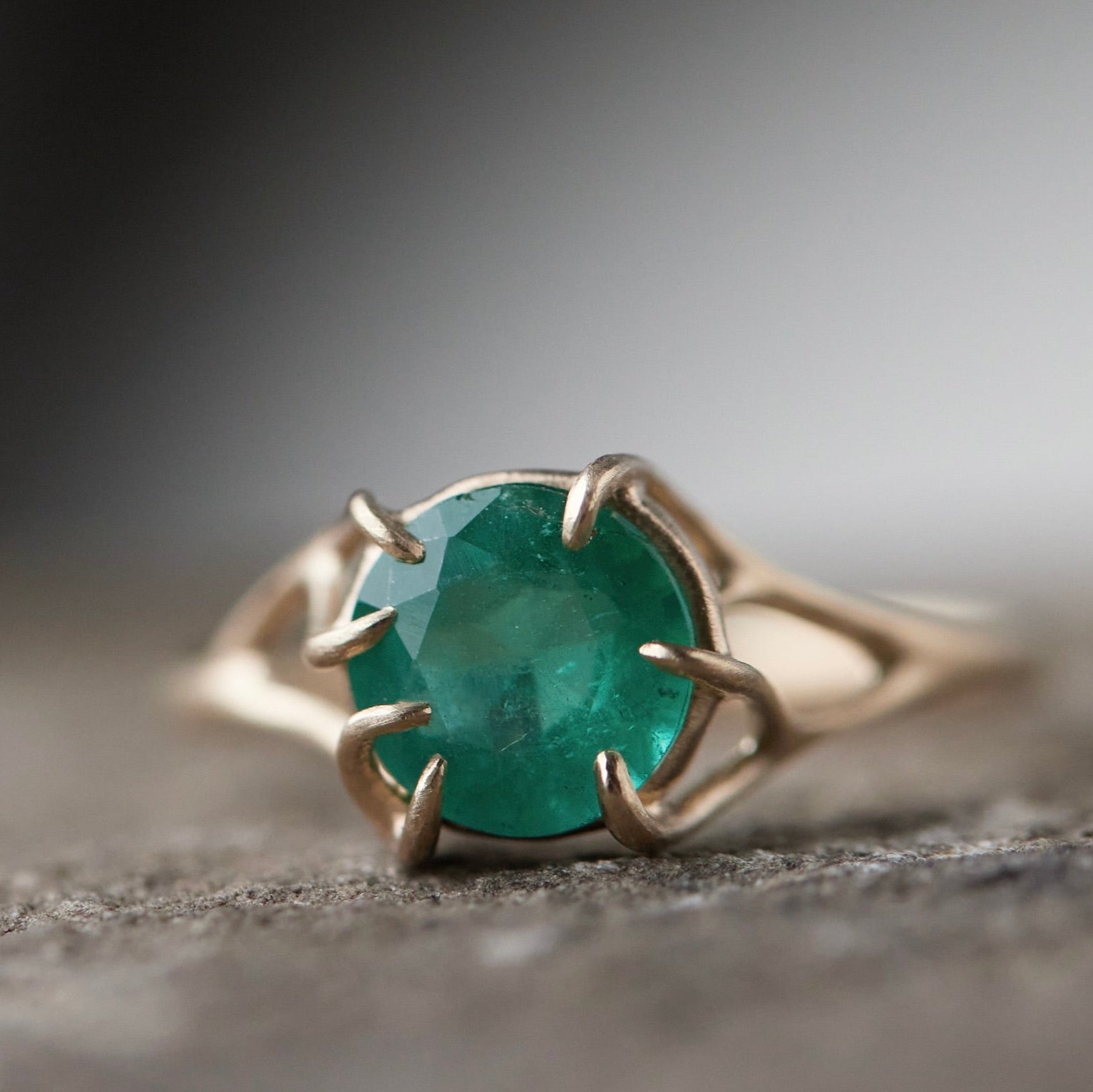 Round green emerald is set in a branch ring with branchy prongs holding the stone. Photographed on stone. Front view.