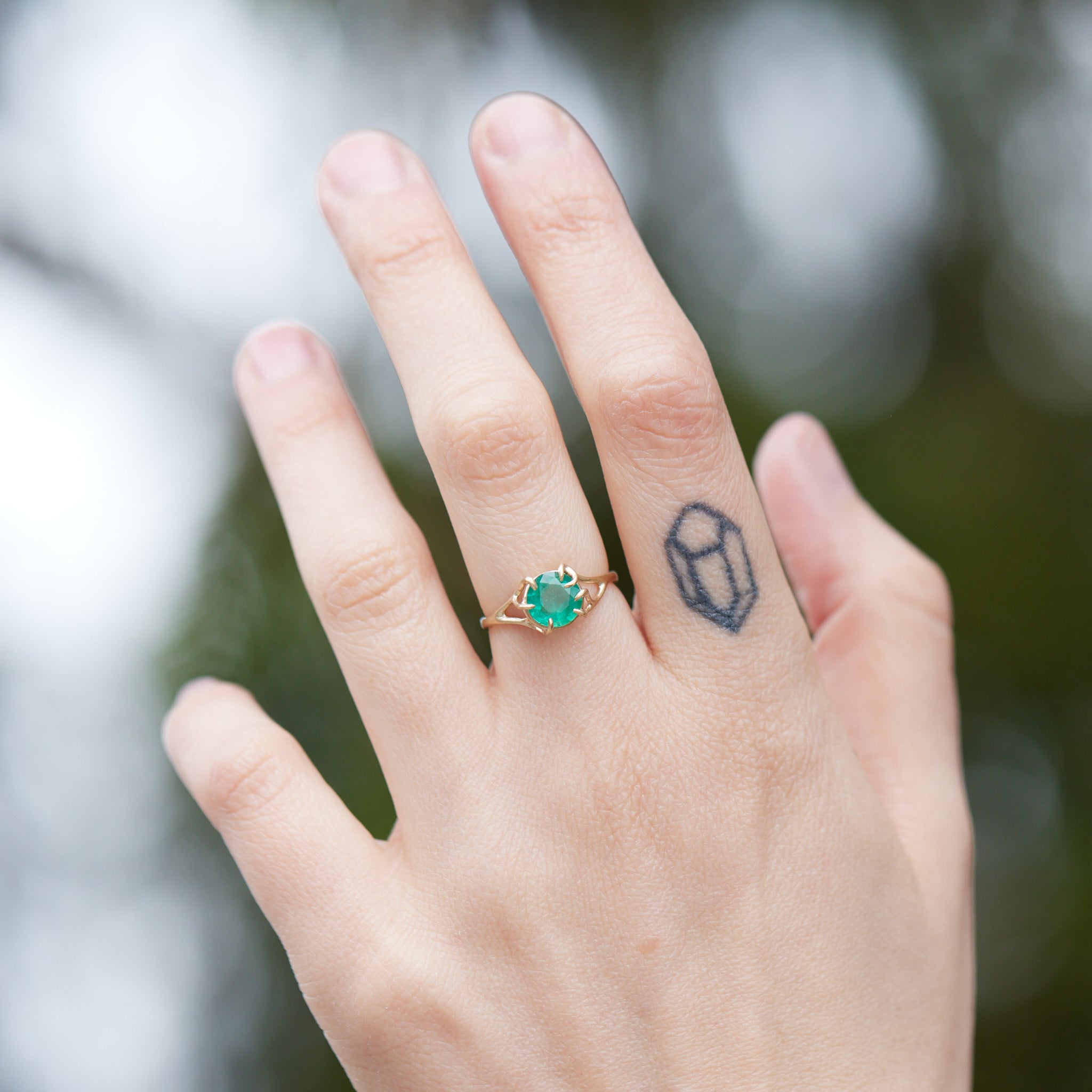 Round green emerald is set in a branch ring with branchy prongs holding the stone. Photographed on person.