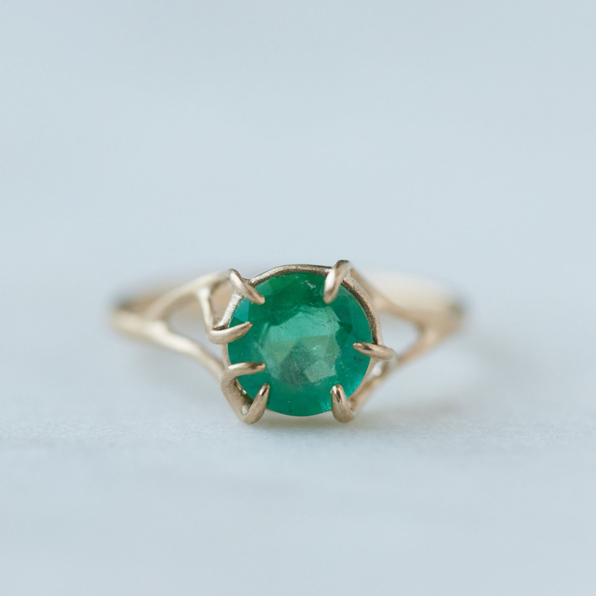 Round green emerald is set in a branch ring with branchy prongs holding the stone. Photographed on stone. Front view.