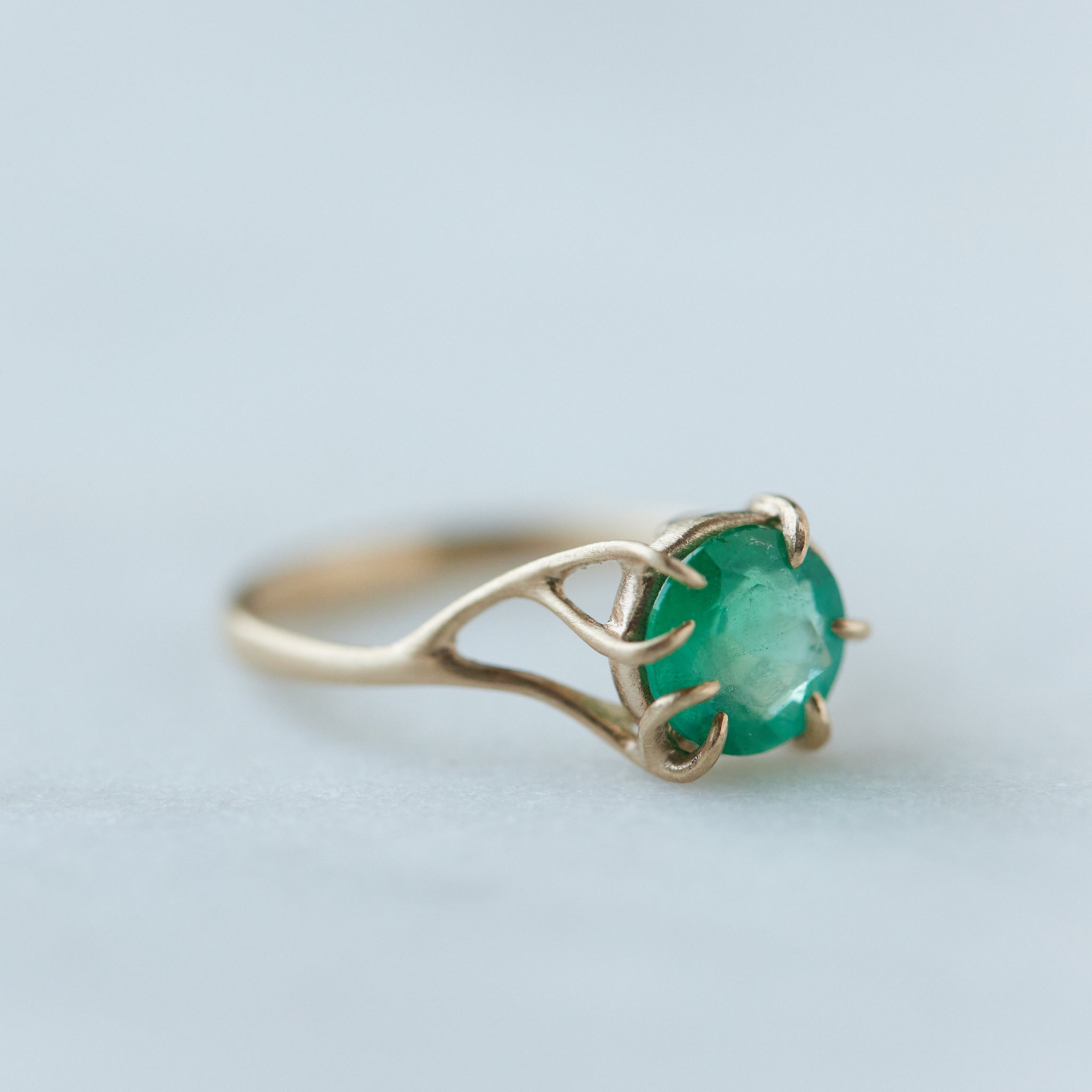 Round green emerald is set in a branch ring with branchy prongs holding the stone. Photographed on stone. Side view.