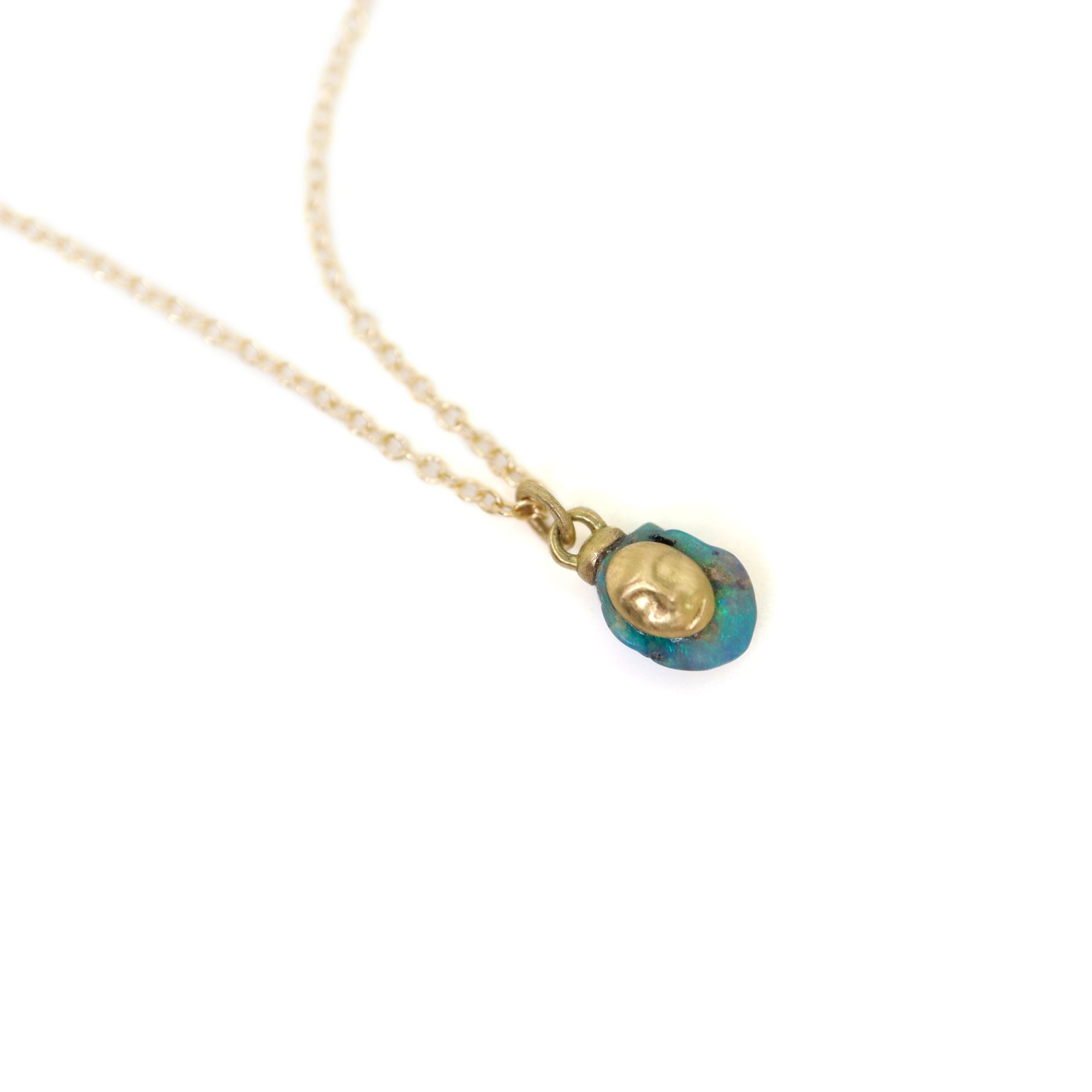 closeup of gold necklace pendant with raw opal featuring a gold face against white, by hannah blount