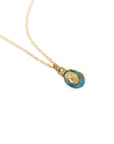 closeup of gold necklace pendant with raw opal featuring a gold face against white, by hannah blount