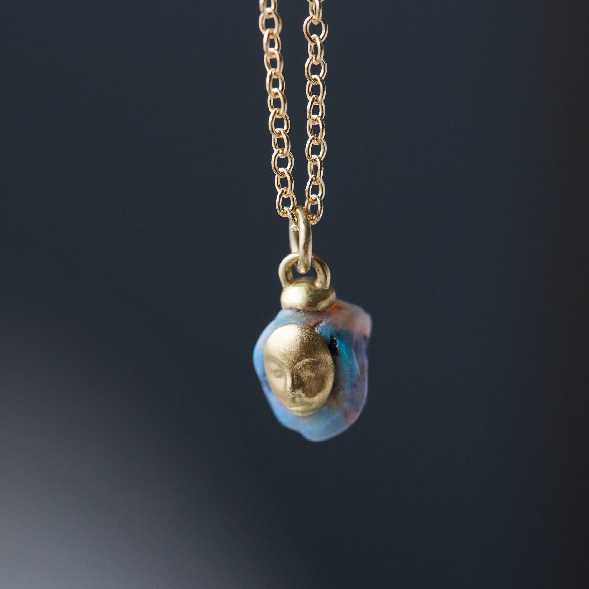 closeup of raw opal with gold face and gold chain against dark background by hannah blount