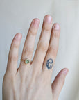 Hand wearing a ring with a green gemstone on a plain background