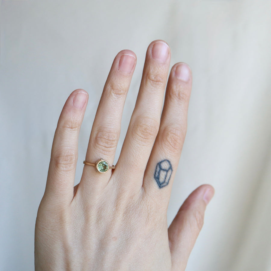 Hand wearing a ring with a green gemstone on a plain background