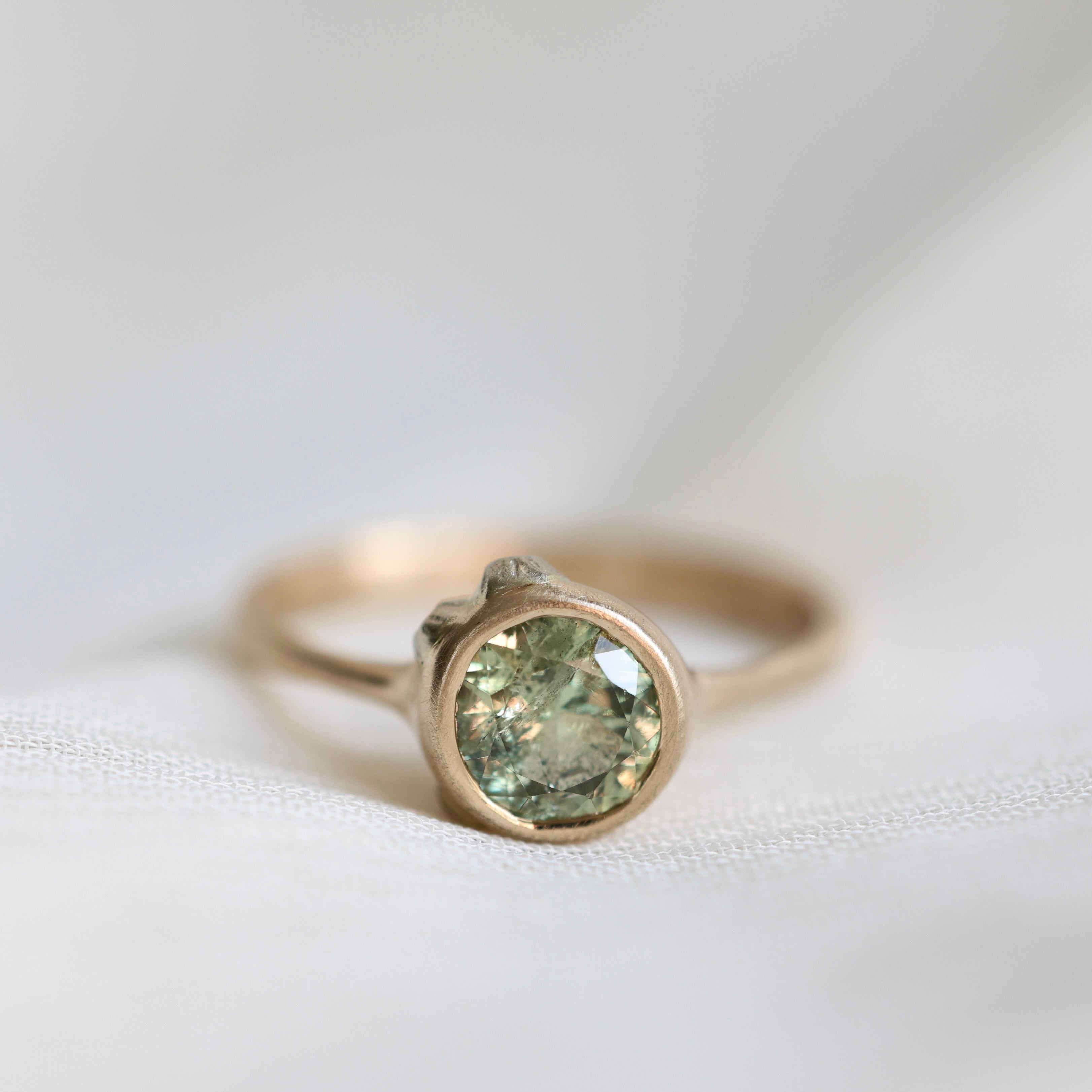 Gold ring with a green gemstone on a white fabric background